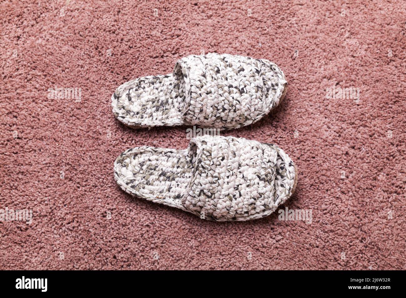 Des pantoufles blanches en maille faites à la main se tiennent sur un tapis rose, photo de gros plan Banque D'Images