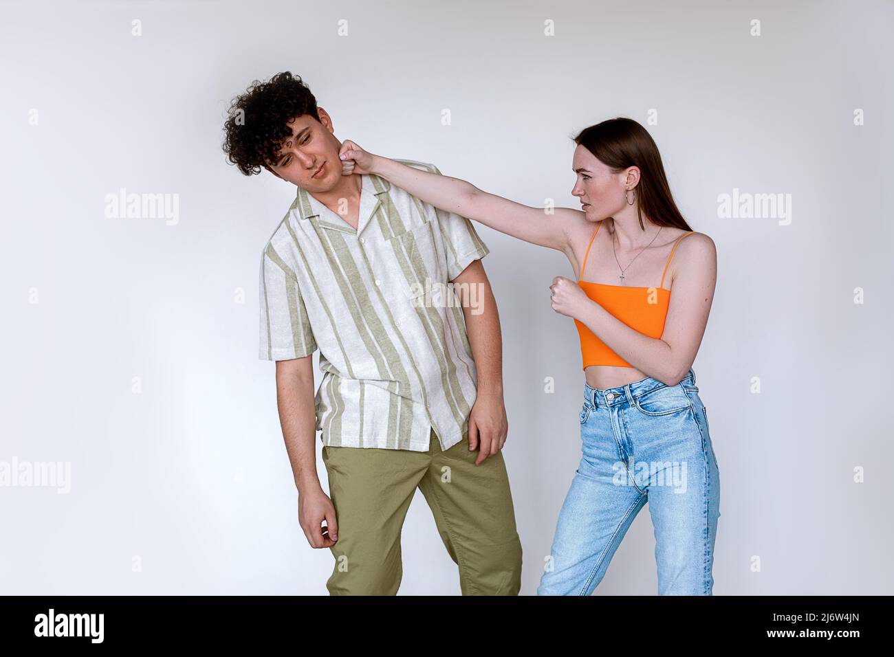 Portrait d'un jeune couple posé sur fond blanc. Une jeune femme en colère déplaisa poinçonner contre un homme fatigué épuisé. Banque D'Images
