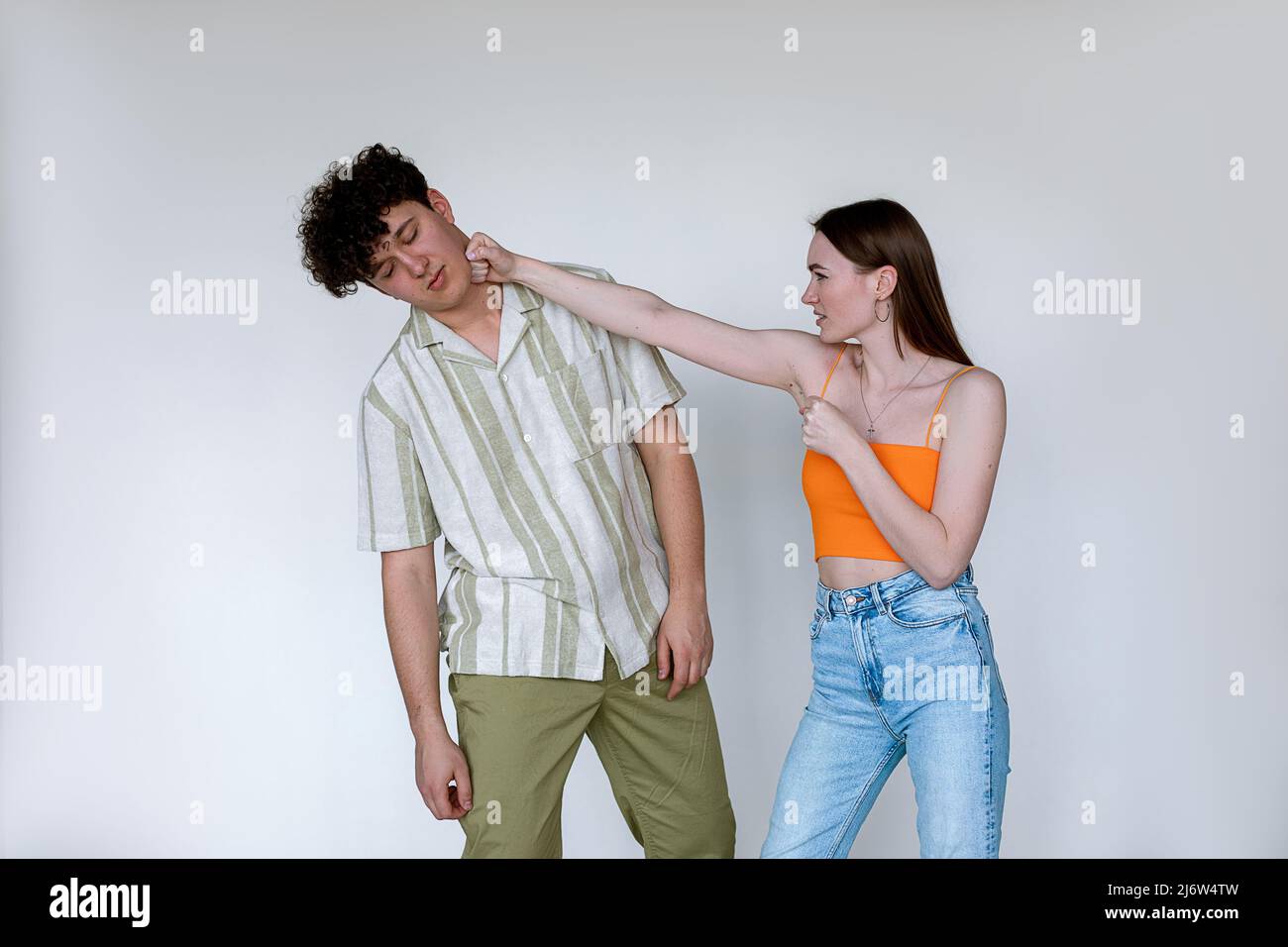 Portrait d'un jeune couple posé sur fond blanc. Jeune femme mécontente de poinçonner un homme évanoui avec les yeux fermés. Banque D'Images