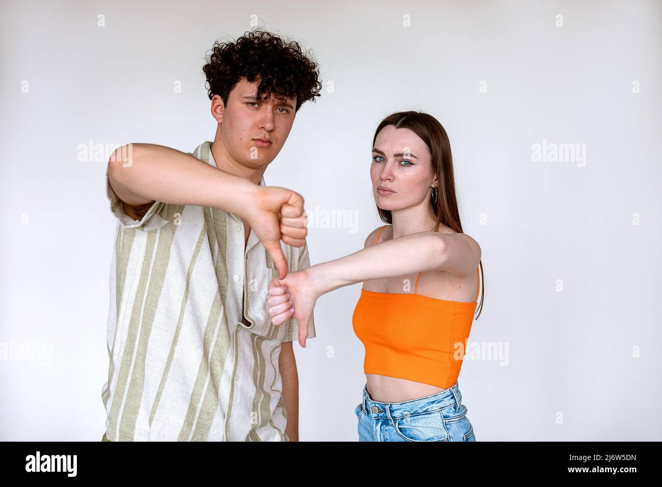 Portrait de jeunes couples mécontents posant sur fond blanc. Jeune contrarié malheureux homme, femme montrant le pouce vers le bas signe. Banque D'Images