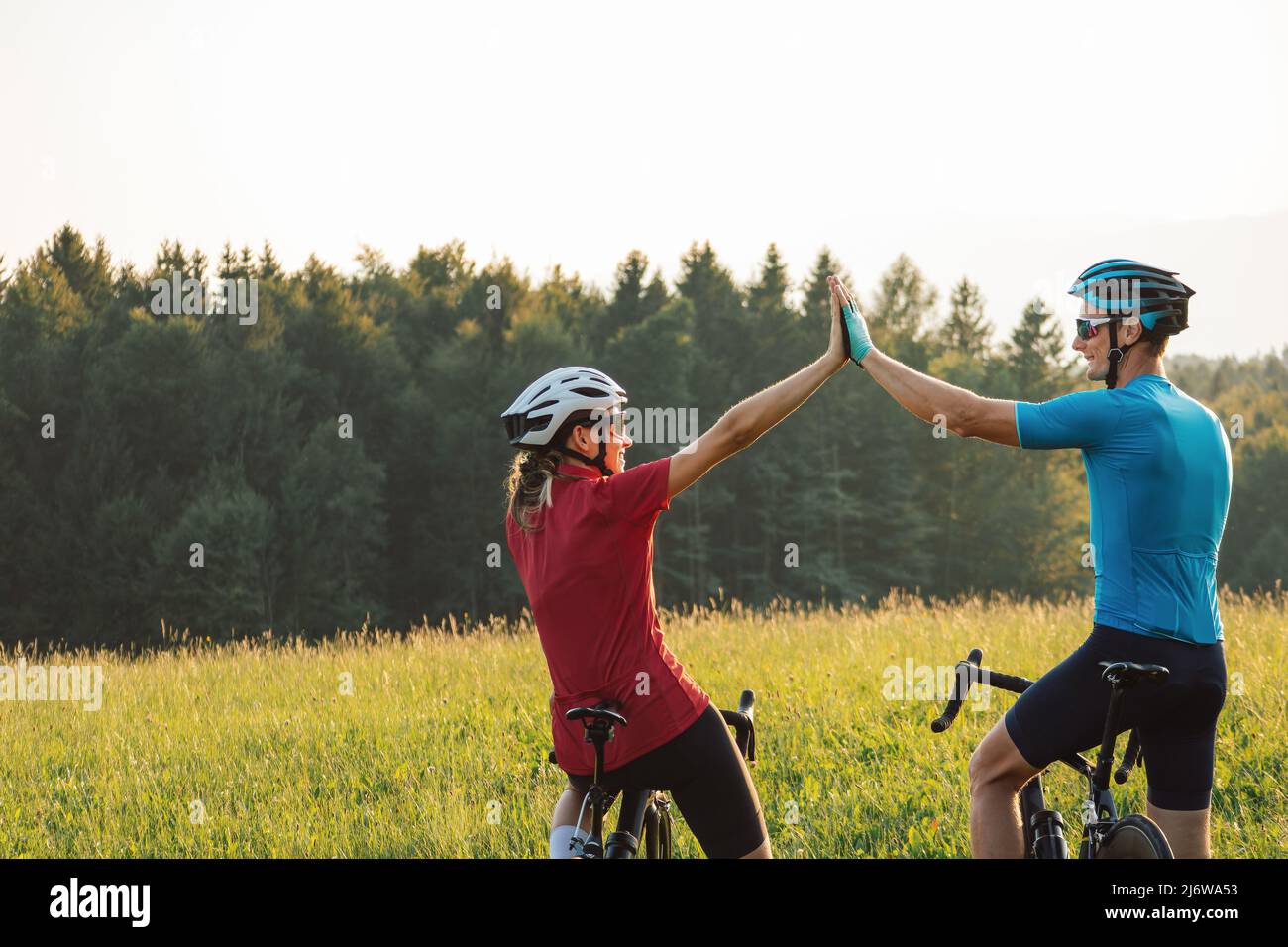 Femme et homme sur des cycles de course sur route prenant une pause après un entraînement réussi et regardant le coucher de soleil sur les montagnes donnant élevé cinq Banque D'Images