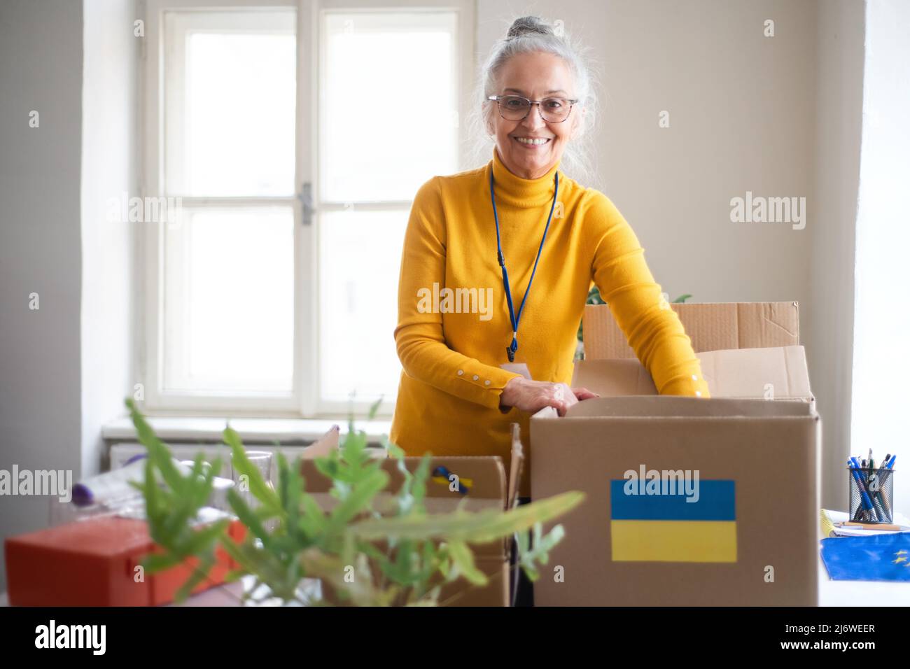 Une femme volontaire senior emballant une boîte avec une aide humanitaire pour les réfugiés ukrainiens en fonction Banque D'Images