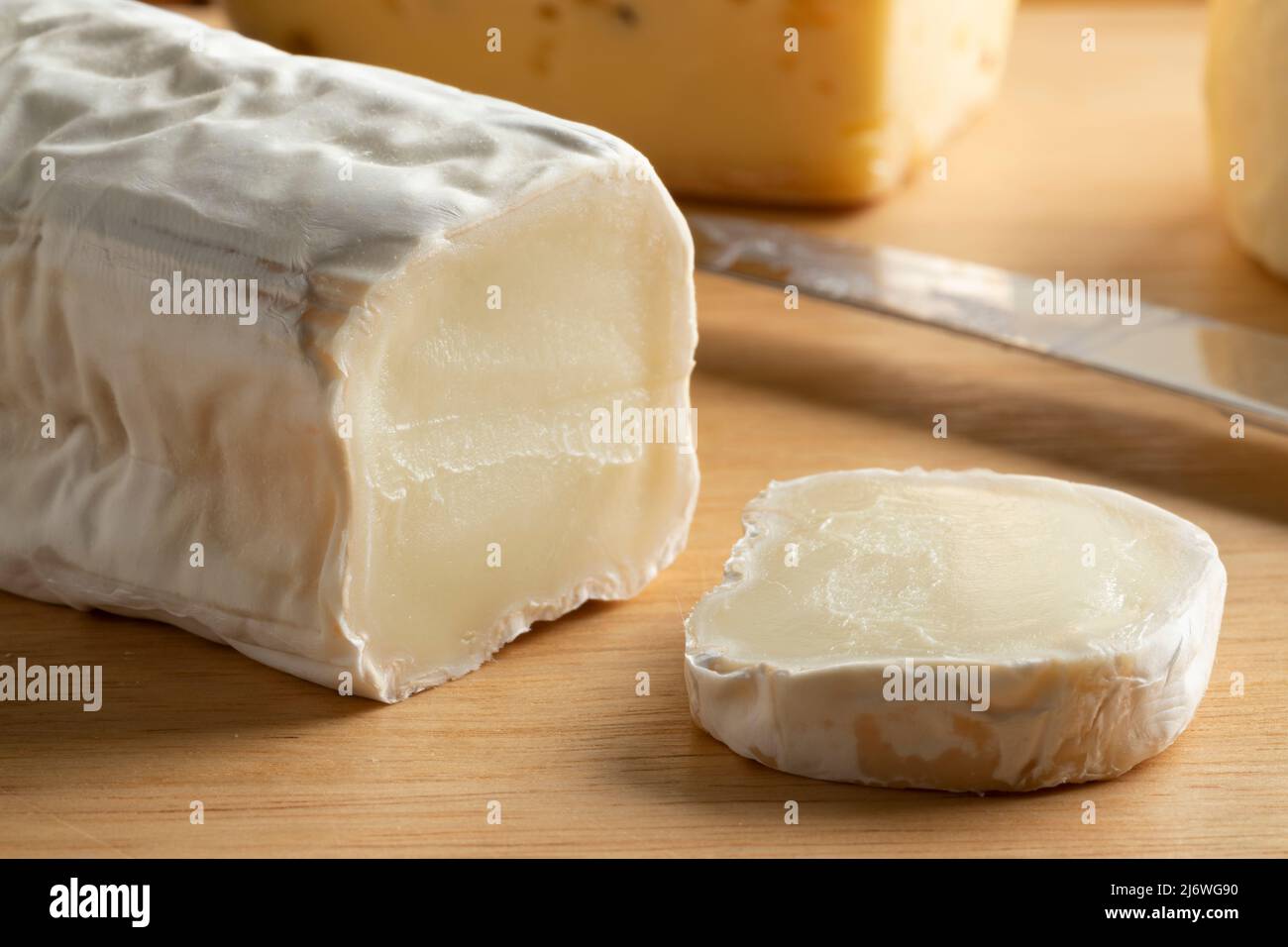 Buche de Chevre, fromage de chèvre, avec une croûte blanche et une tranche sur une planche à découper Banque D'Images