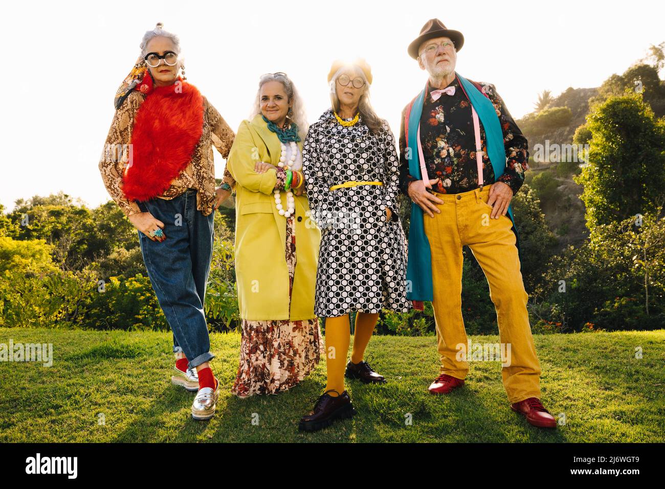 Quatre amis âgés confiants debout dans un parc par une journée ensoleillée. Groupe de personnes âgées stylées portant des vêtements décontractés colorés. Ci senior insouciant Banque D'Images