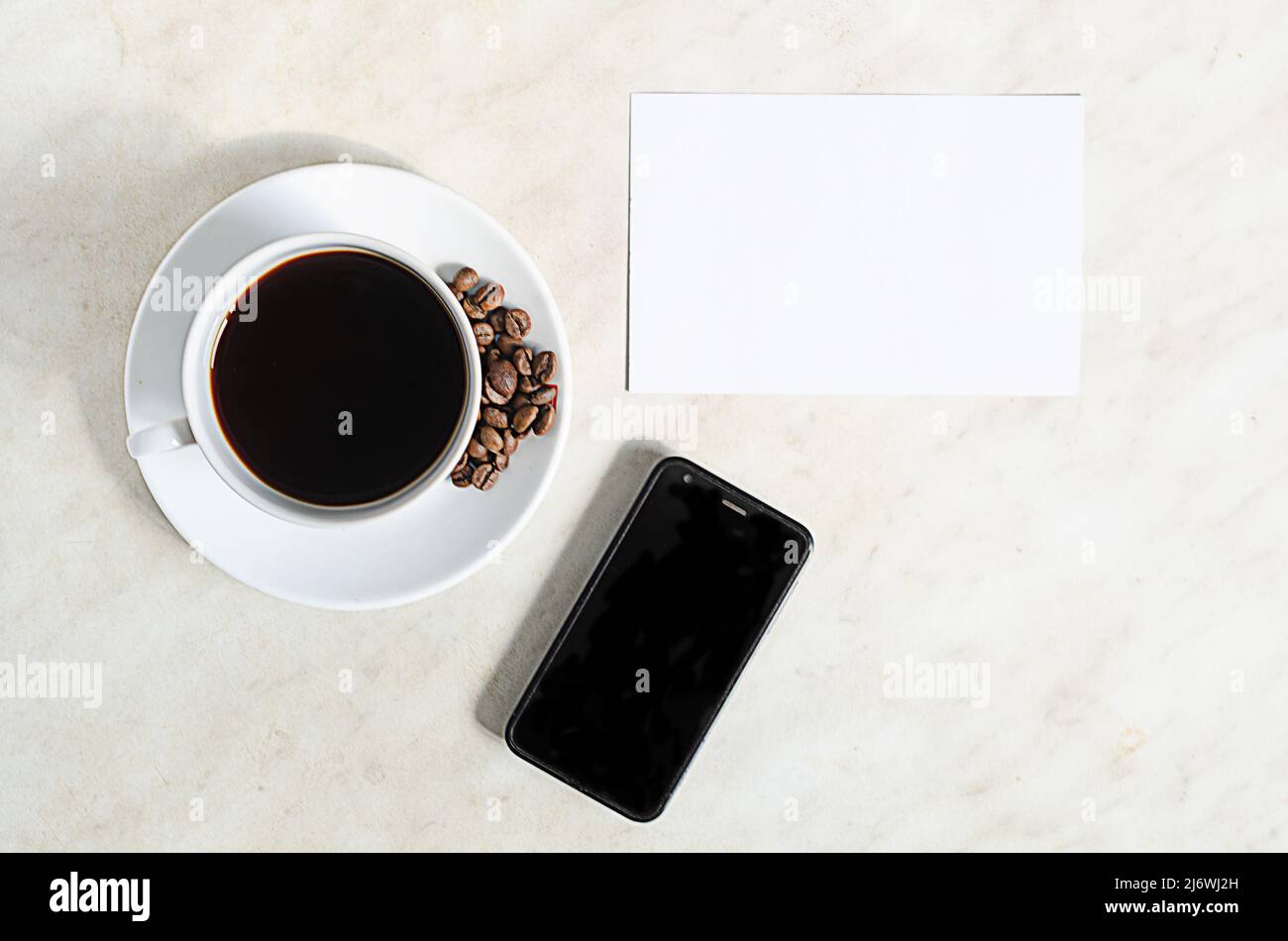 Une tasse de café avec des grains de café, un téléphone portable et un blanc vide sur la table Banque D'Images