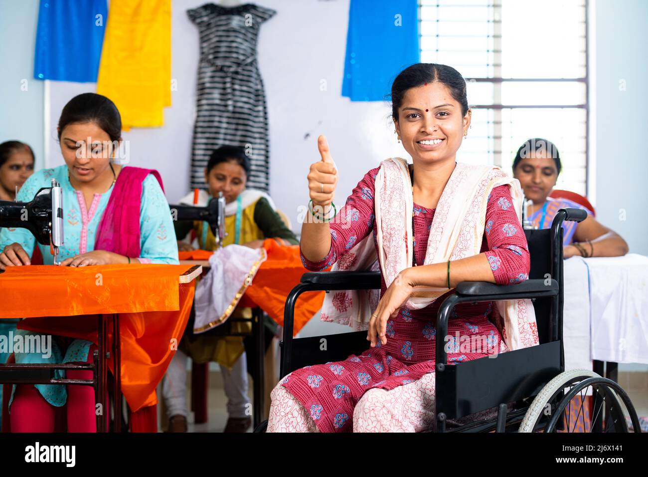 Femme souriante heureuse avec un handicap montrant le pouce vers le haut geste sur les vêtements en fauteuil roulant - concept de propriétaire de petite entreprise, inspiration et Banque D'Images