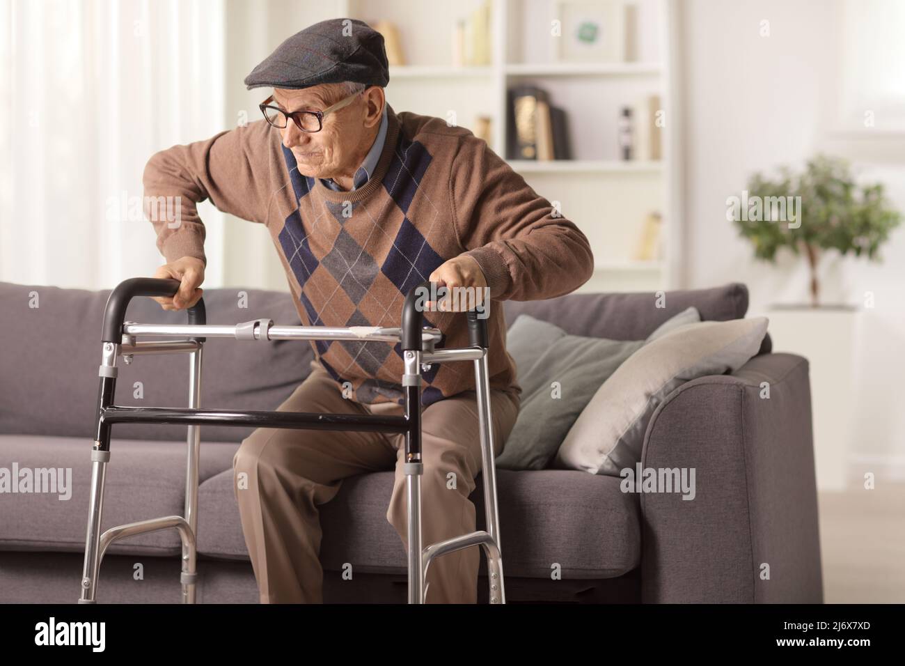 Homme âgé sur un canapé essayant de marcher avec un marcheur à la maison Banque D'Images