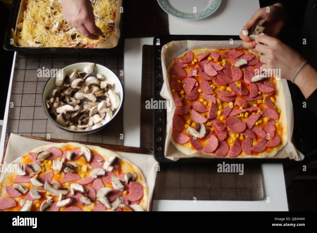 Permet de déconcentrer les ingrédients de la pizza sur la pâte. Homme en cuisine. Sauce tomate rouge, saucisses, maïs doux, champignons, fromage. Pizza maison. Base de Margarita. Hom Banque D'Images