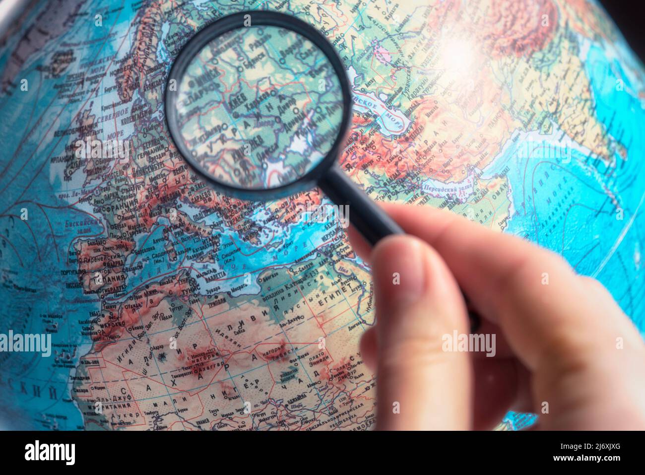 Main avec loupe zoom Ukraine sur la carte du monde avec la langue russe. Banque D'Images