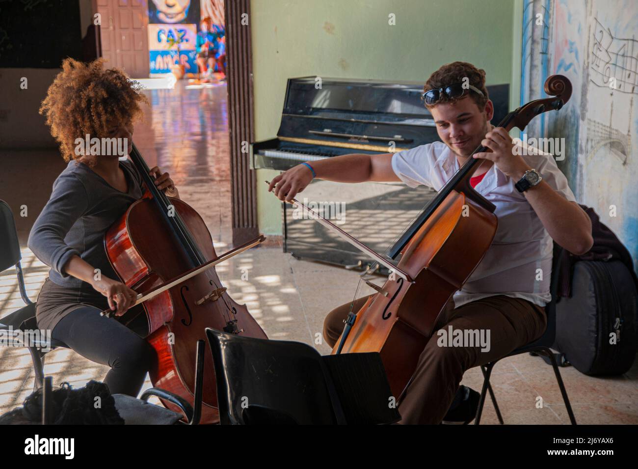 Les jeunes élèves répètent jouer le violoncelle dans une école de Matanzes, Cuba, avec un tableau de John Lennon et Yoko Ono sur le mur derrière eux. Banque D'Images