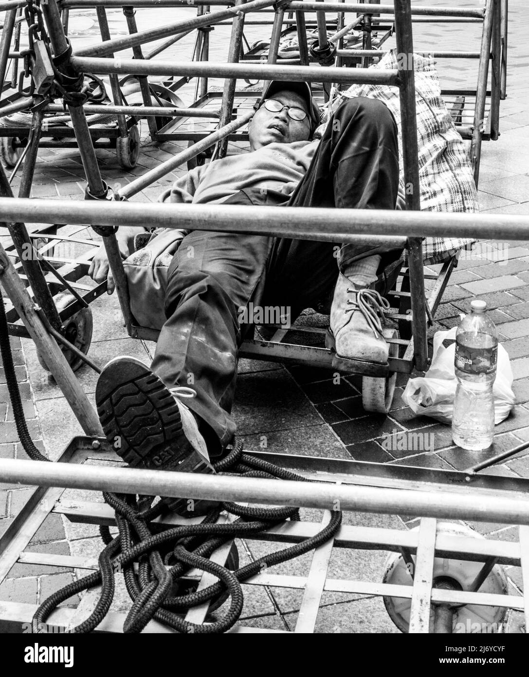 Un ouvrier prend une pause et dort en trolleys dans une rue de Hong Kong. Banque D'Images