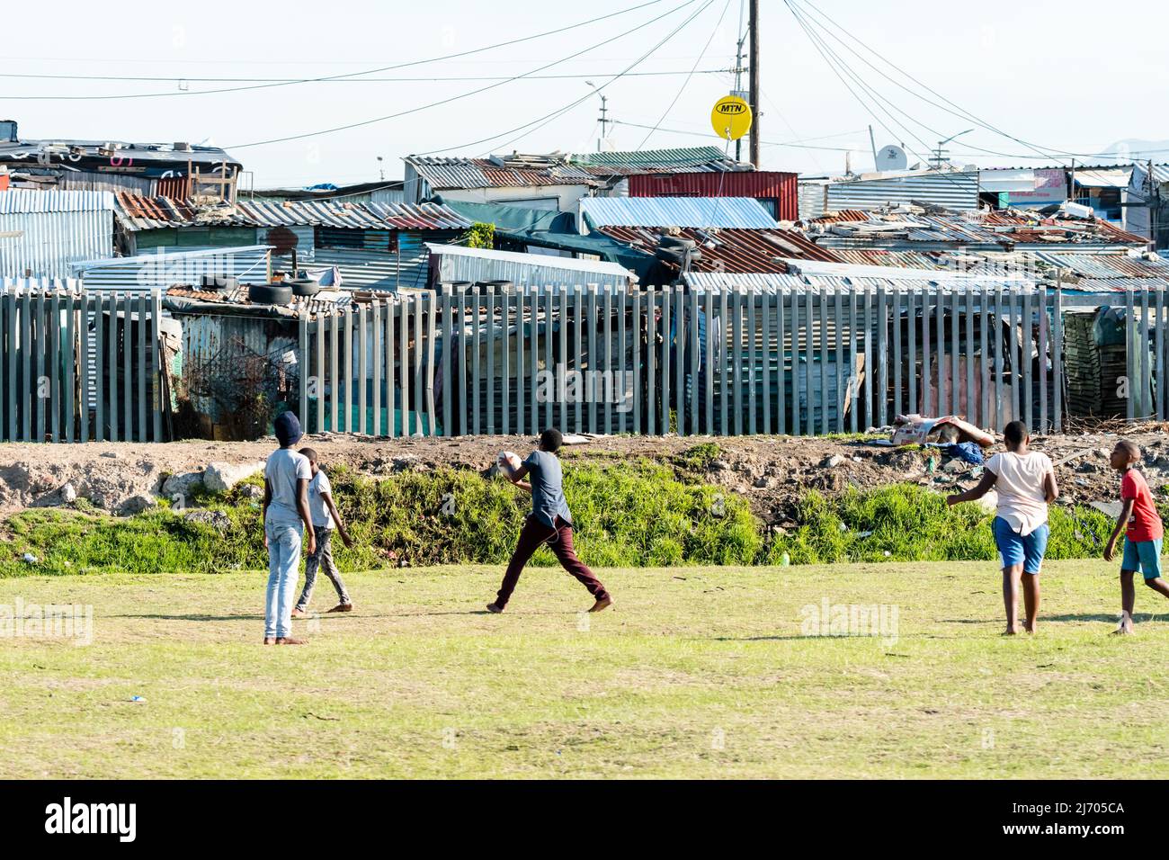 Des enfants ou des enfants d'Afrique noire jouant au rugby avec un groupe d'amis devant leurs maisons ou leurs cabanes dans un canton à l'extérieur du Cap, en Afrique du Sud Banque D'Images