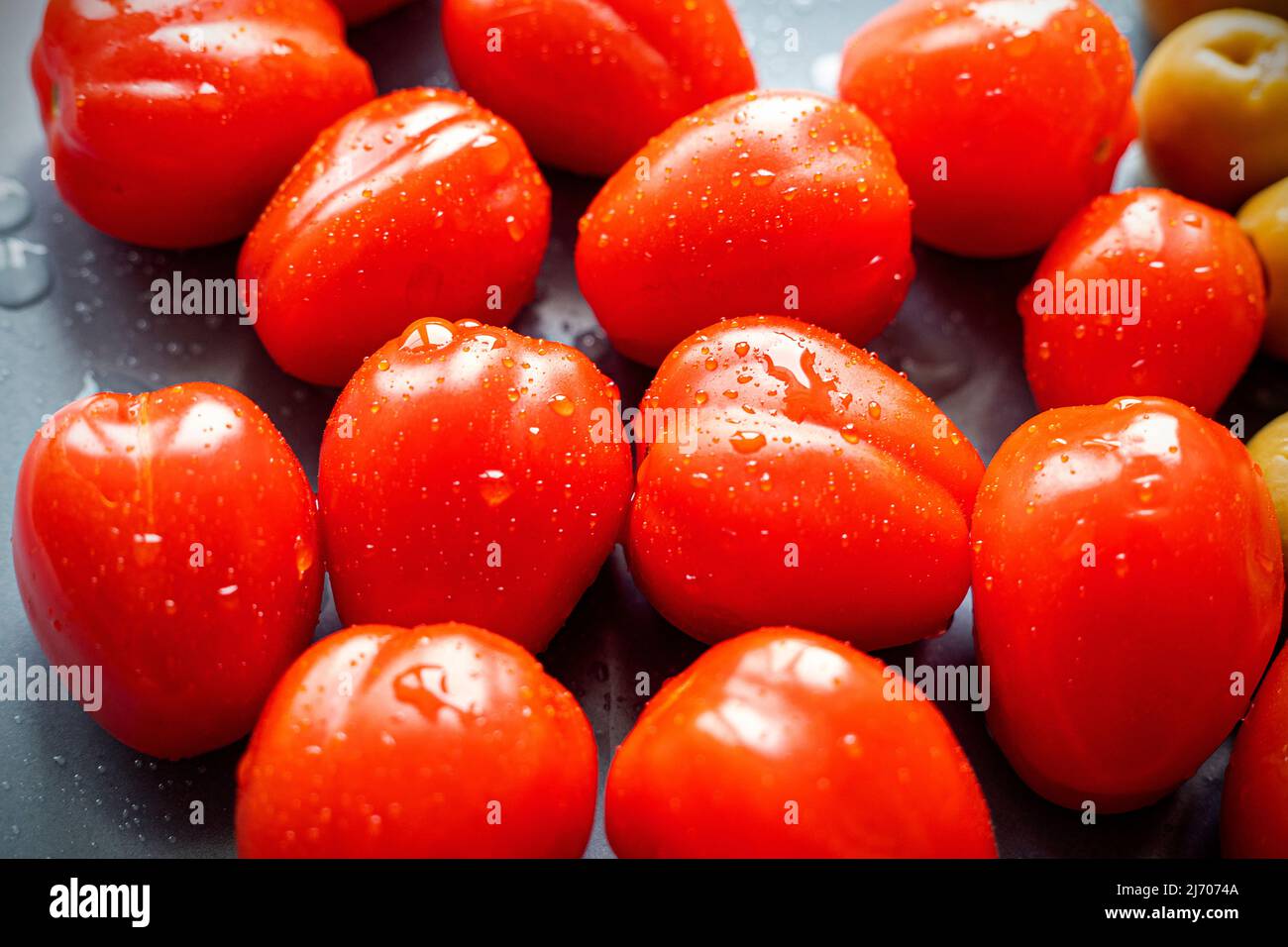 Groupe de tomates cerises mûres humides avec des gouttes sur une assiette noire, vue du dessus Banque D'Images