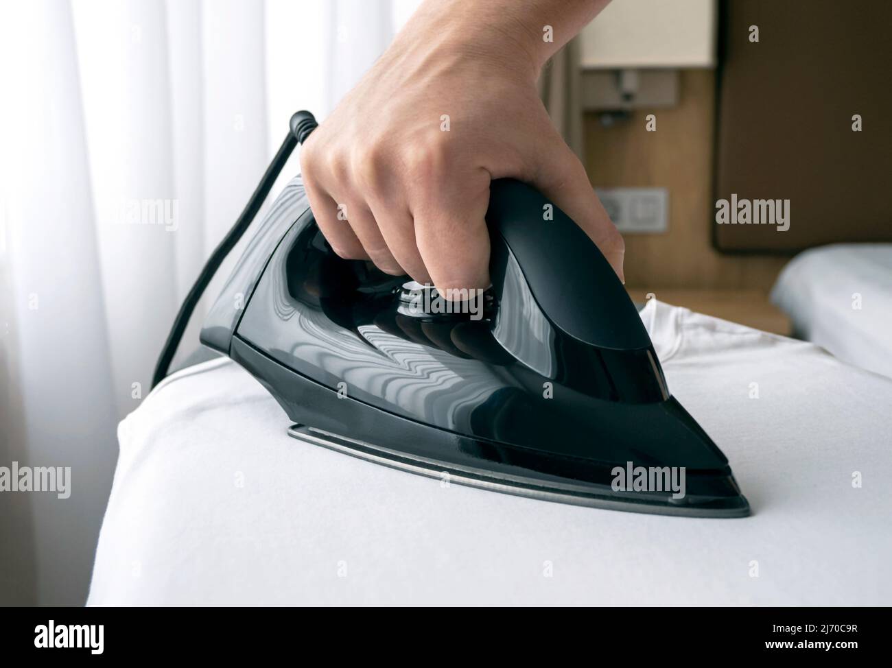 Gros plan de la main avec un fer noir sur la planche pendant le repassage Banque D'Images