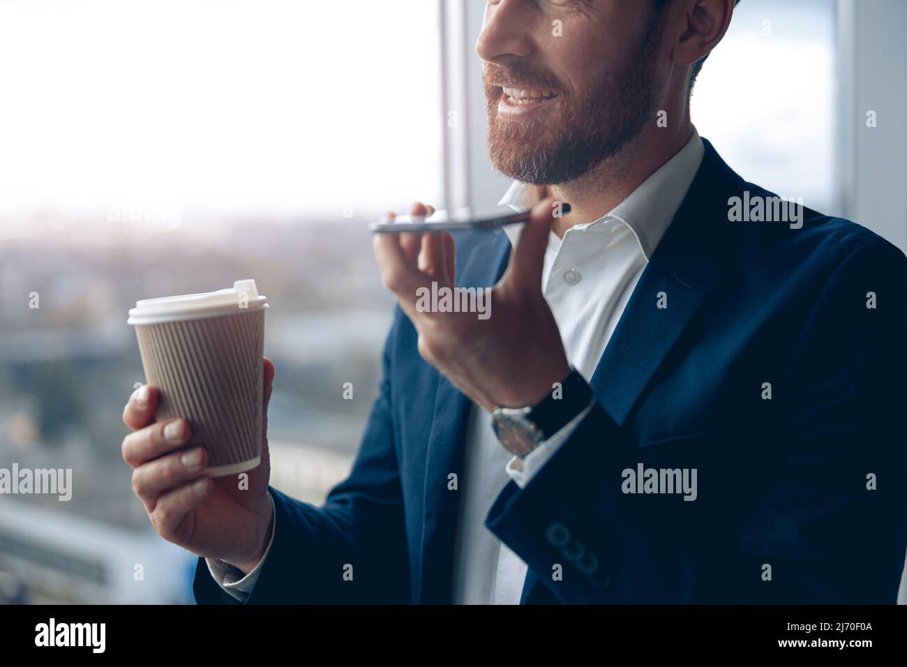 homme d'affaires utilisant un smartphone pour enregistrer un message vocal à son partenaire commercial et boire du café Banque D'Images