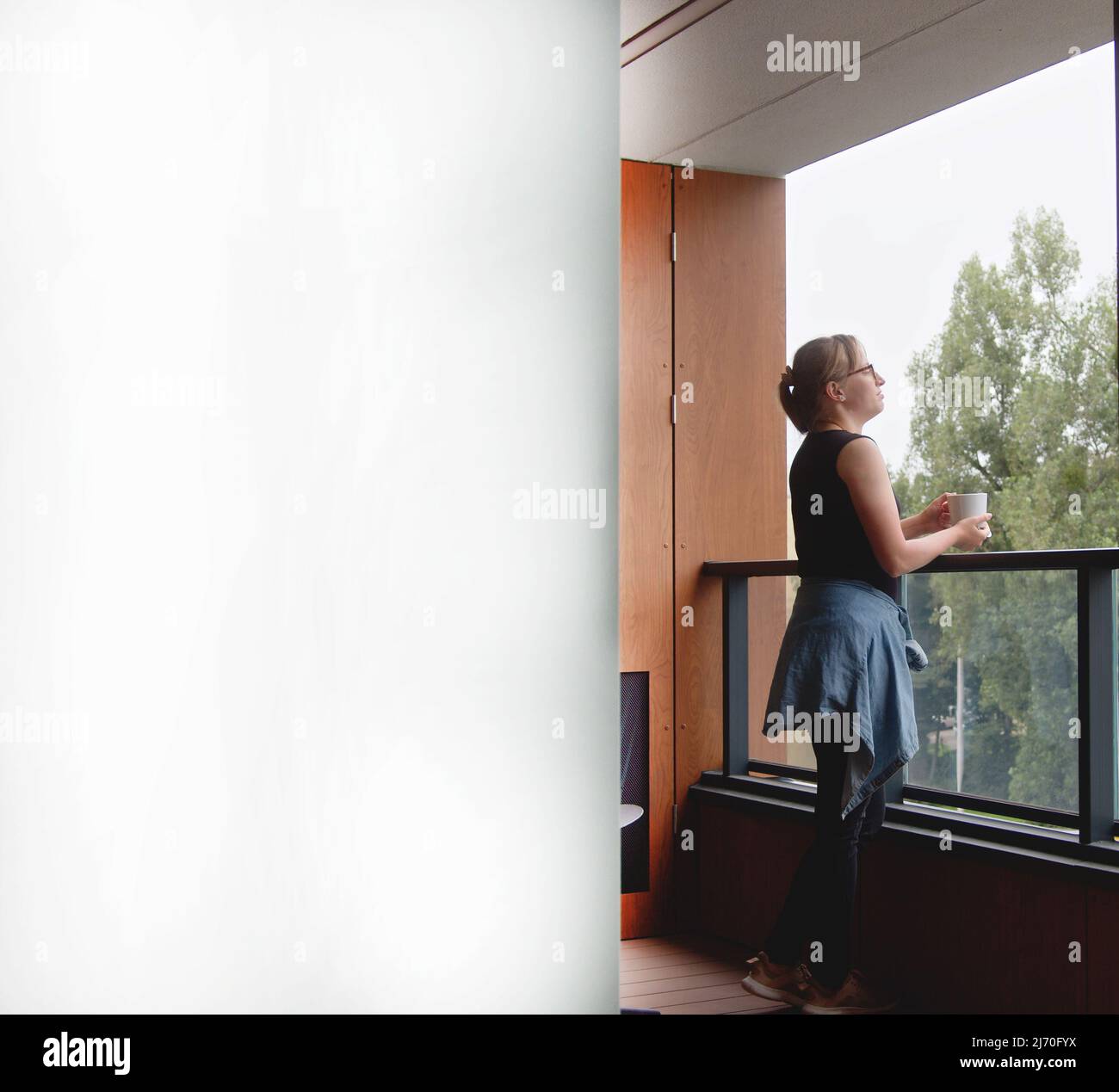 Cliché carré d'une femme caucasienne debout sur son balcon, tenant une tasse de thé ou de café. La moitié de la photo est blanche. Copier l'espace. Photo de haute qualité Banque D'Images