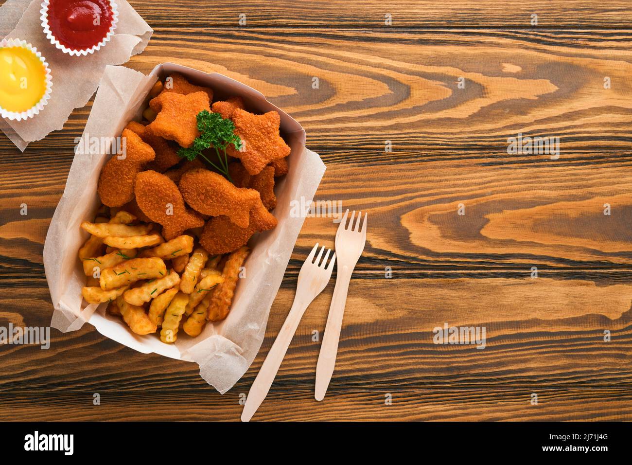Fish and Chips, restauration rapide britannique. Bâtonnets de poisson avec frites sur une assiette en papier à emporter sur un fond de table en bois. Traditionnel anglais Banque D'Images