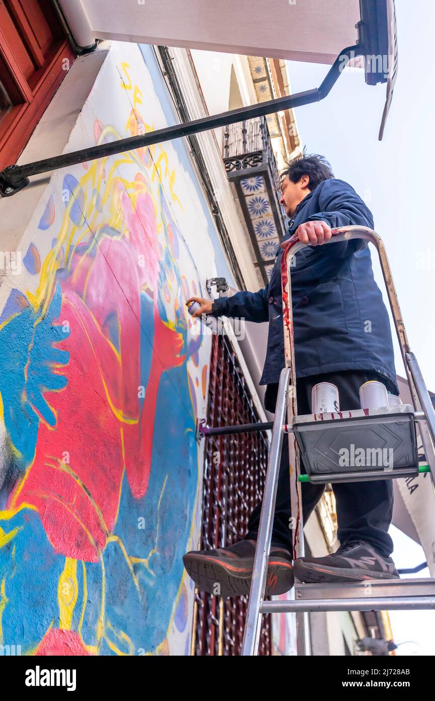 Un artiste de rue vaporisant de la fresque en restant sur une échelle au mur du restaurant Donde da la vuelta el viento, Lavapiez, Madrid, Espagne Banque D'Images