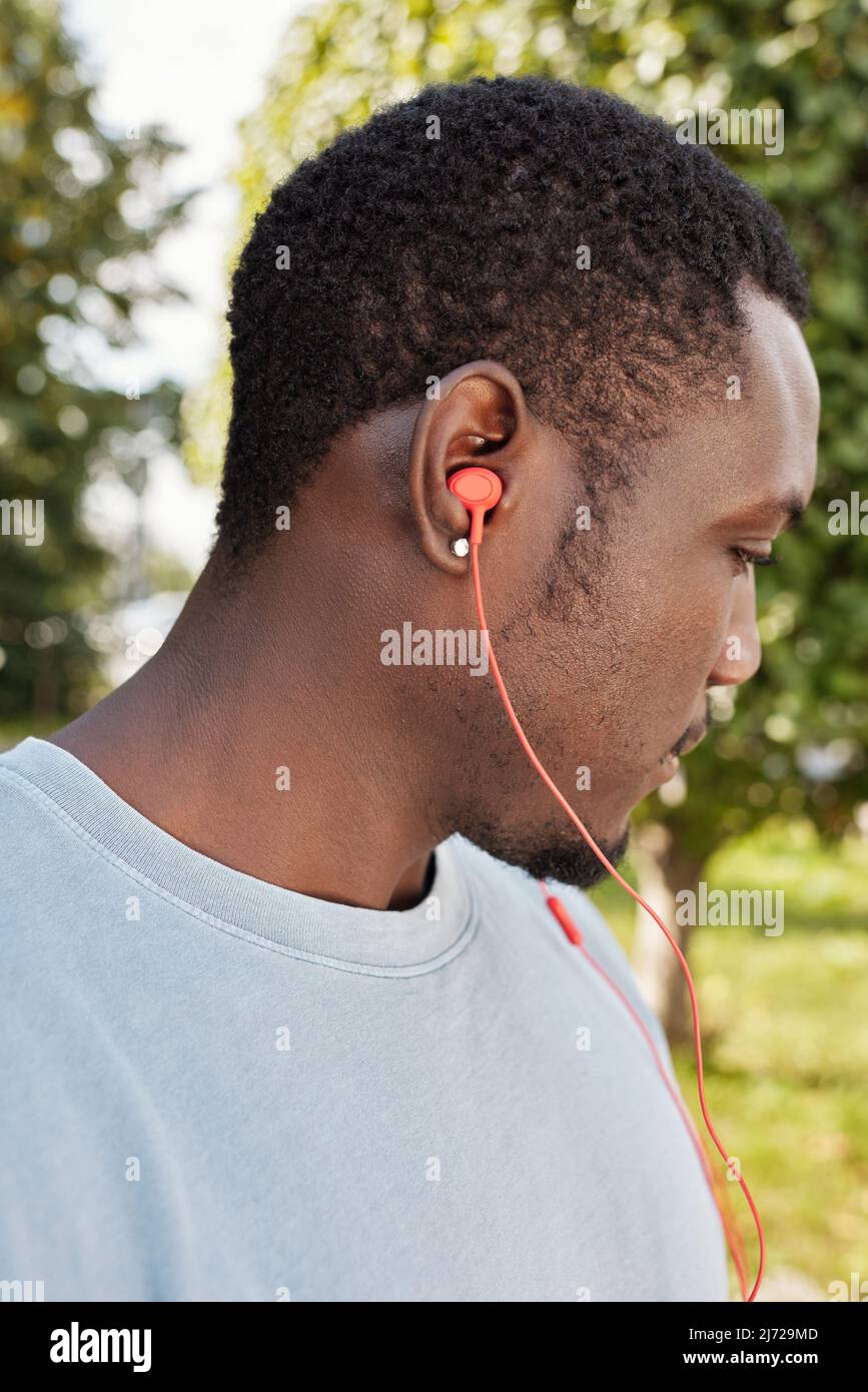 Portrait de profil d'un jeune homme afro-américain portant des boucles d'oreilles écoutant de la musique à l'extérieur par des écouteurs Banque D'Images