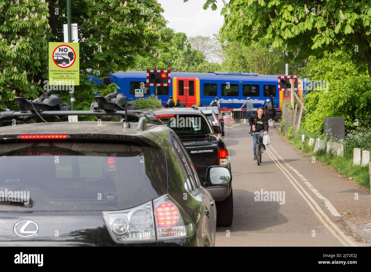 Des voitures stationnaires faisant la queue et tournant au ralenti tandis qu'un train South Western Railway passe la boîte de signalisation de la route Vine de Network Rail à Barnes, Londres, SW13, Angleterre, Royaume-Uni Banque D'Images