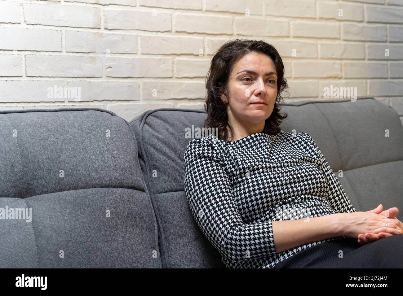 Une femme européenne d'âge moyen aux cheveux foncés est assise sur un canapé Banque D'Images