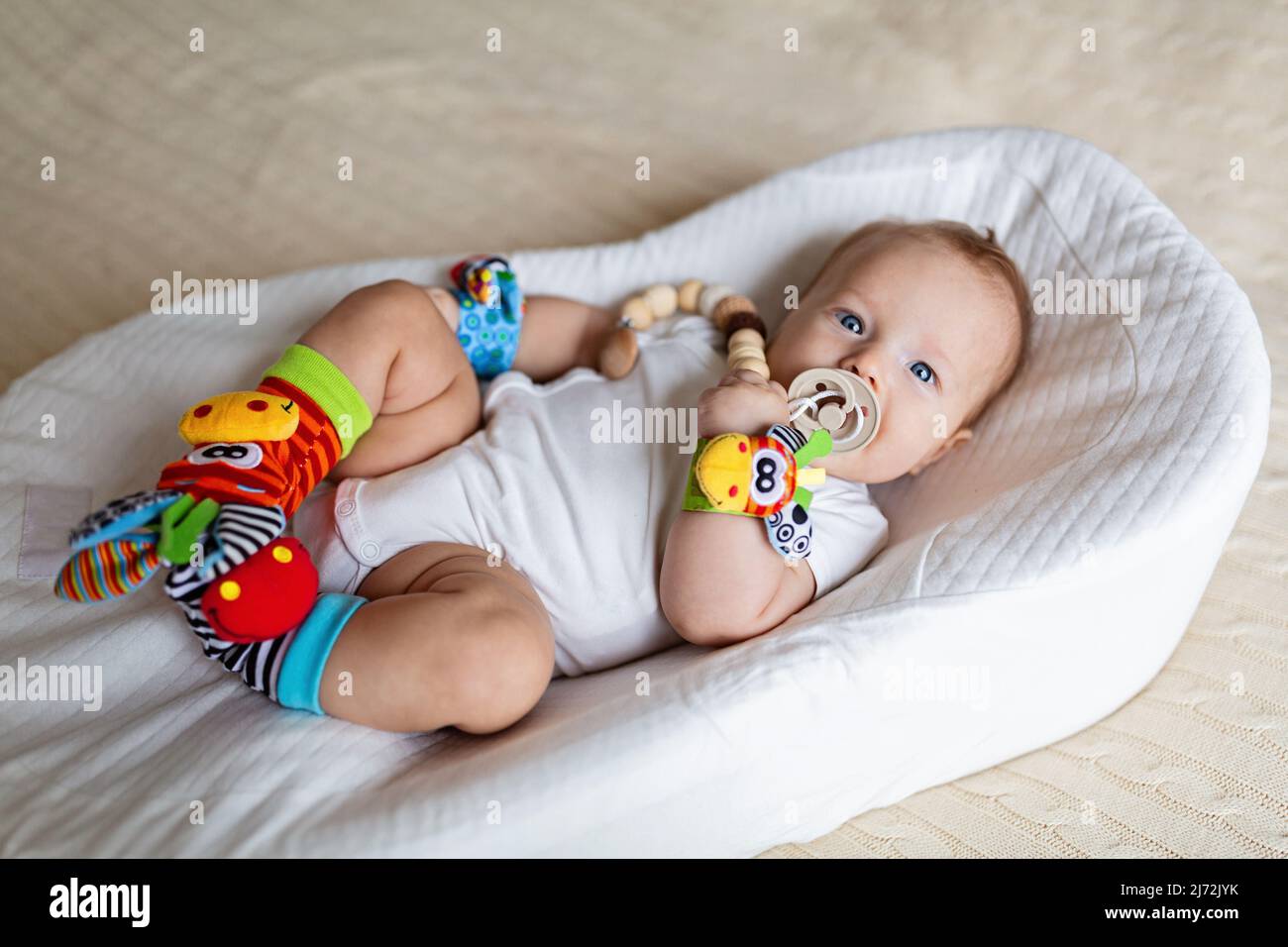 Mignon blanc blanc bébé de trois mois couché dans le cocon à la maison.  Enfant portant sur les mains et les jambes bourré son jouet éducatif, sucer  mamelon Photo Stock - Alamy
