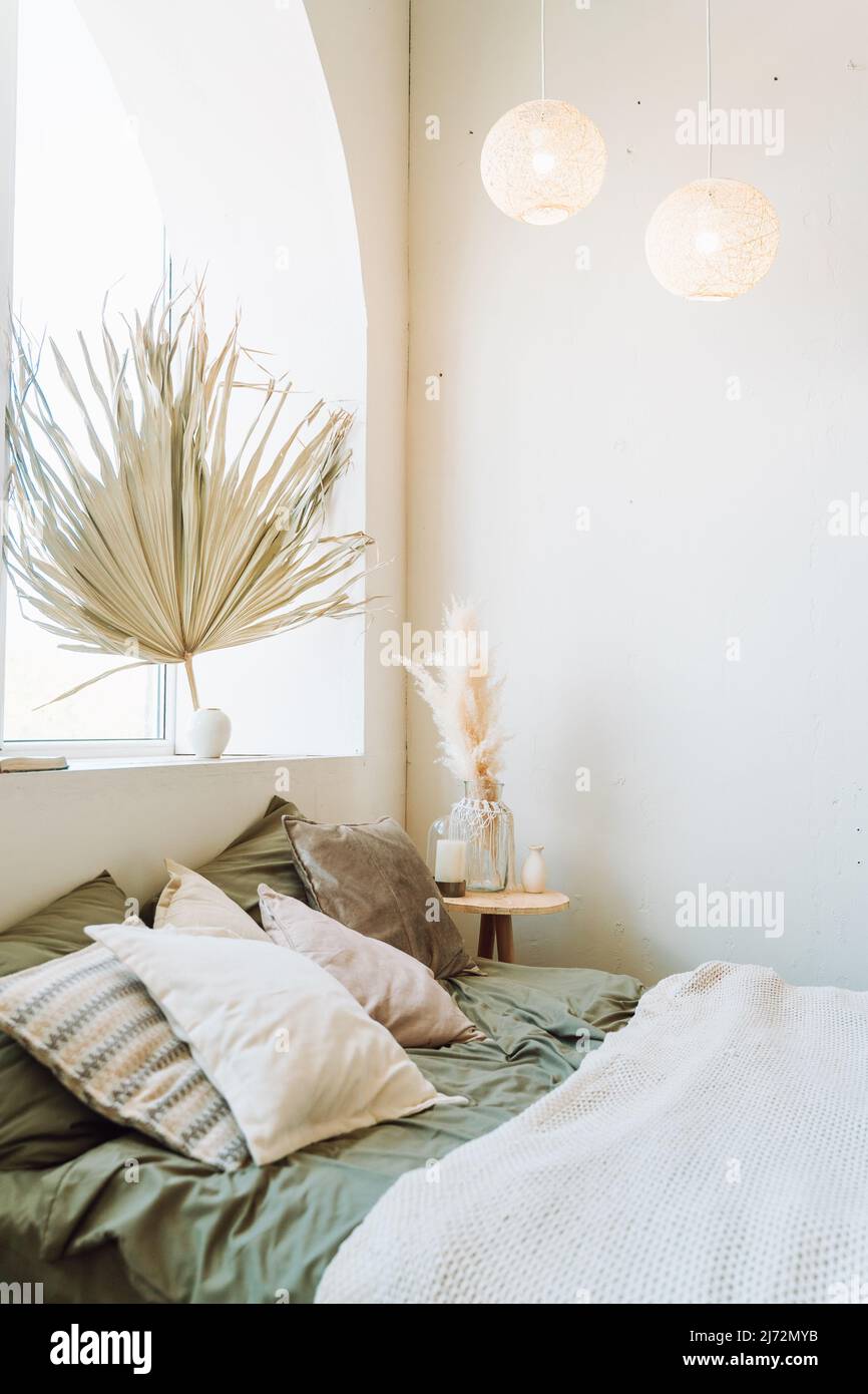 Intérieur de chambre moderne ensoleillée avec lit recouvert de linge de lit gris, écossais beige. Différents vase en verre avec des plantes sèches de pampas sur le lit en bois t Banque D'Images