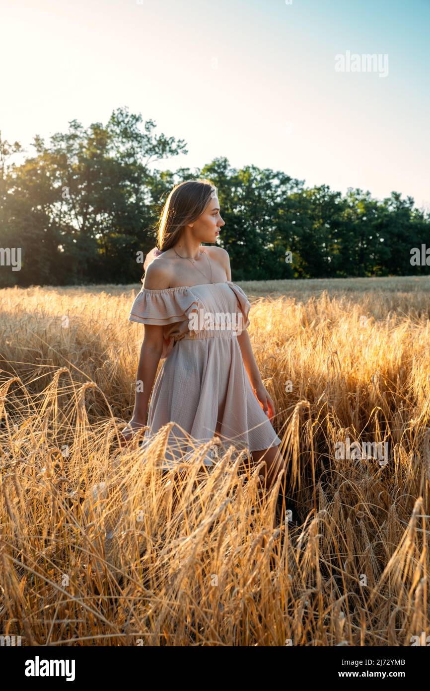 Connectez-vous à la nature, ralentissez, soyez présent, entrez dans vos sens. Paisible seule jeune femme en robe marchant sur le champ de blé au coucher du soleil le jour d'été Banque D'Images