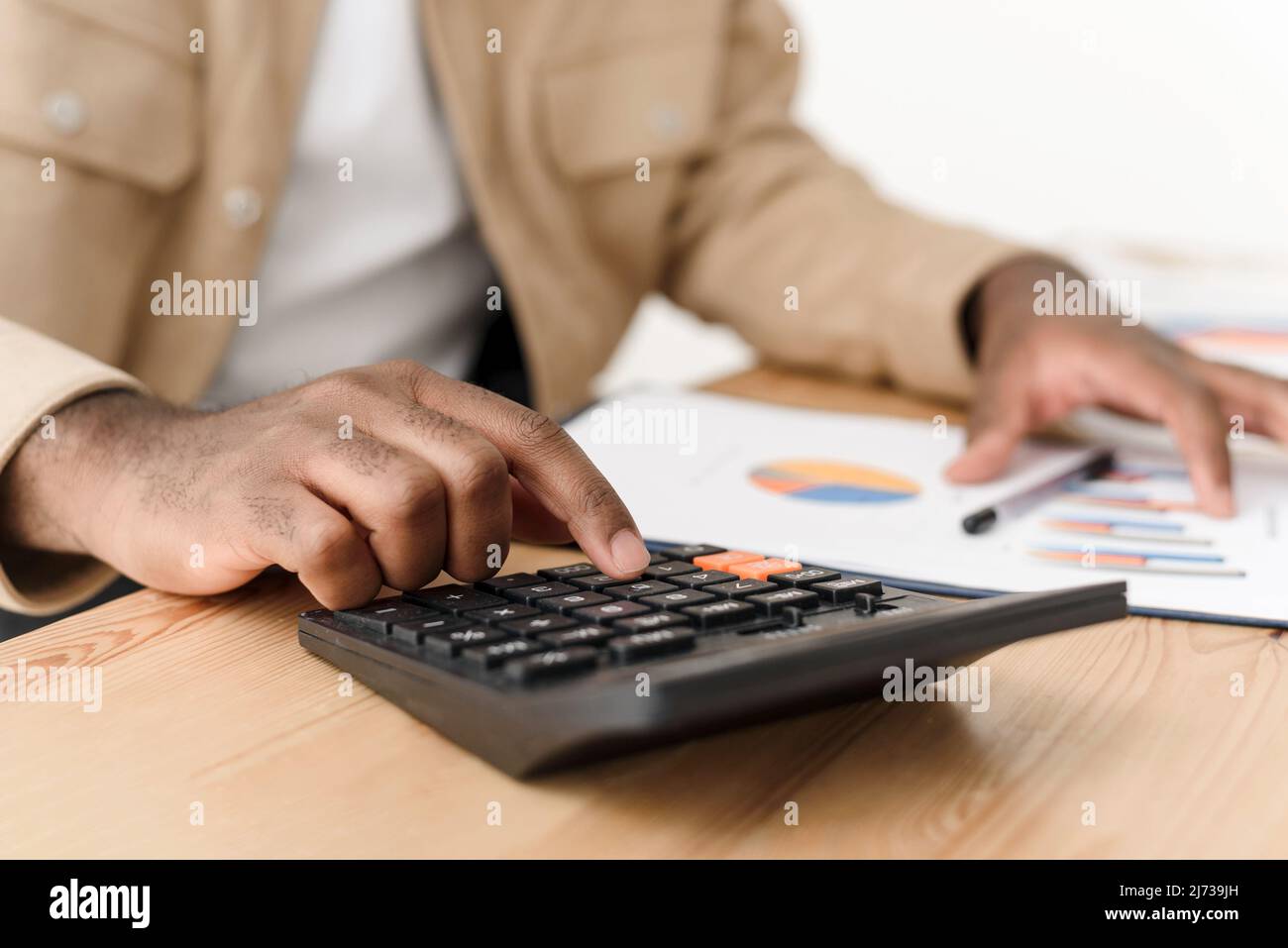 Gros plan est la main d'un homme noir effectuant des calculs sur une calculatrice à la maison. Maintenir le budget d'un ménage, calculer les paiements hypothécaires. Banque D'Images