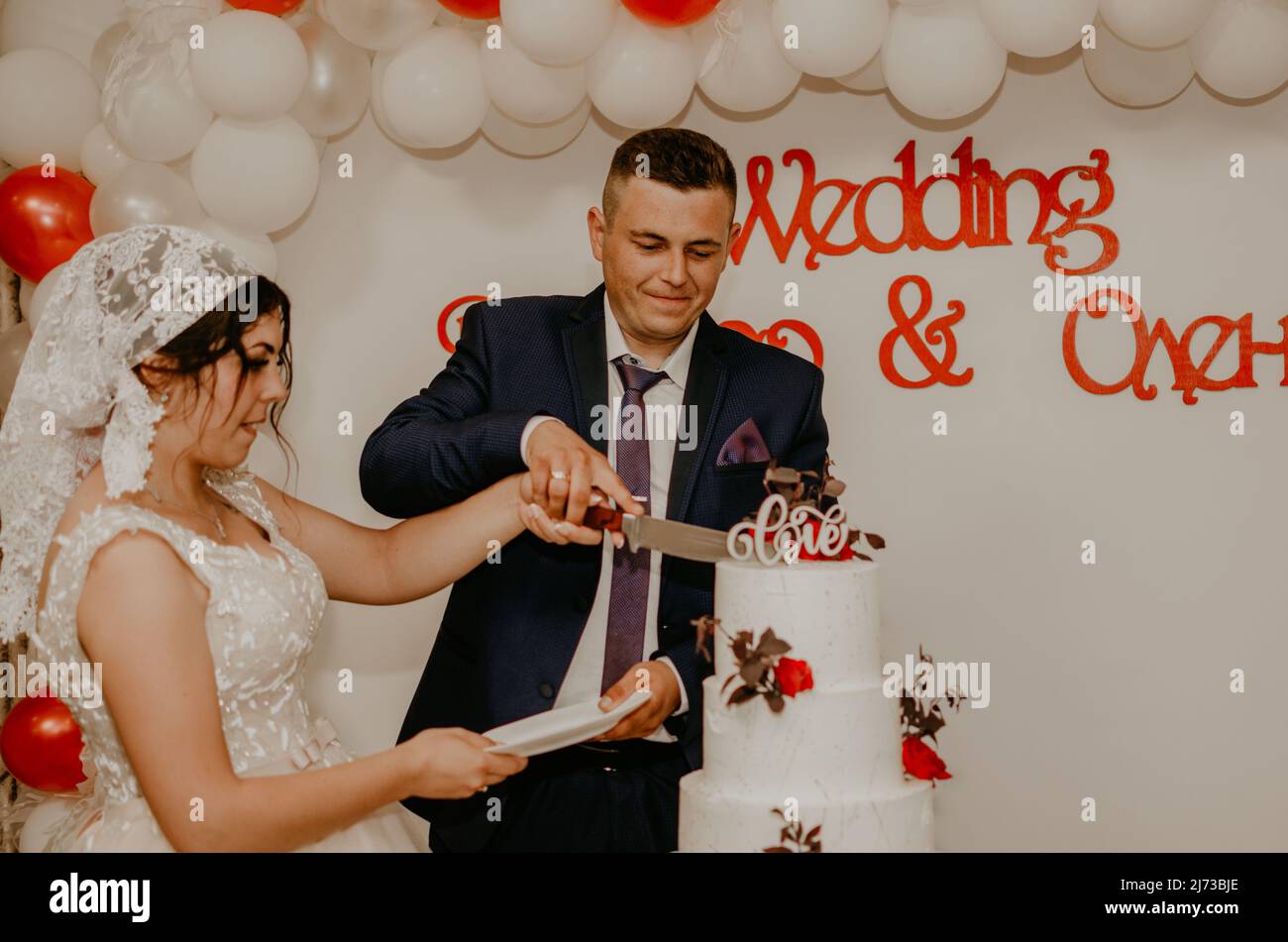 lors du mariage, le marié et la mariée ont coupé leur grand gâteau blanc à plusieurs niveaux et ont le goût qu'ils ont nourri l'un de l'autre. Traditions russes ukrainiennes slaves Banque D'Images