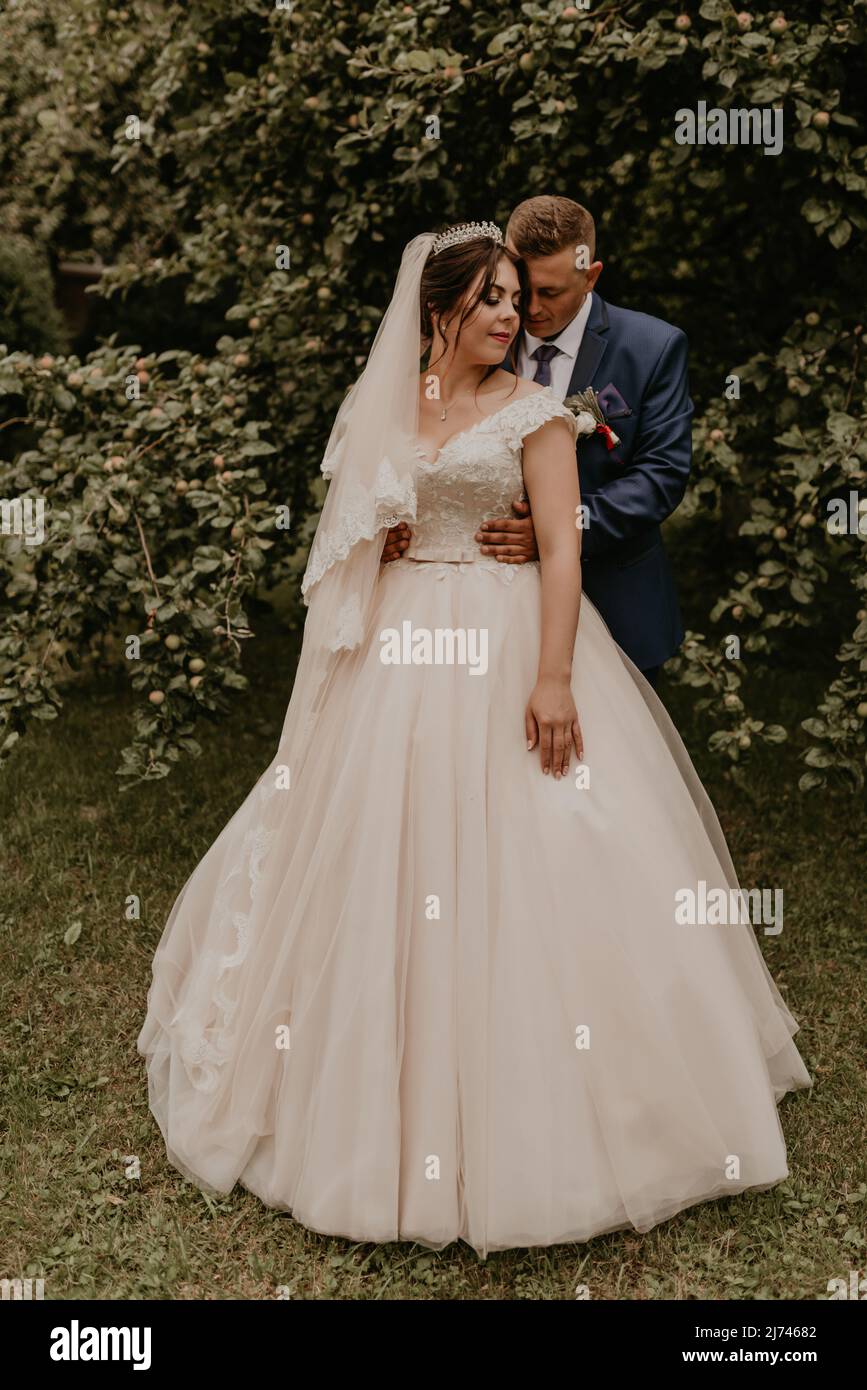 Blonde européenne caucasien jeune homme marié en costume bleu et femme à cheveux noirs mariée en robe de mariage blanche avec voile long et tiara sur la tête. Newlyweds Banque D'Images