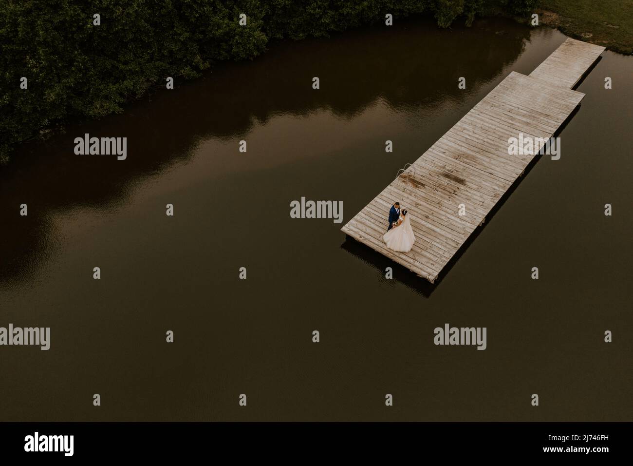 Homme caucasien européen marié en costume et femme à cheveux noirs mariée en robe de mariage blanche avec voile long et tiara sur la tête. Les jeunes mariés s'embrasent Banque D'Images