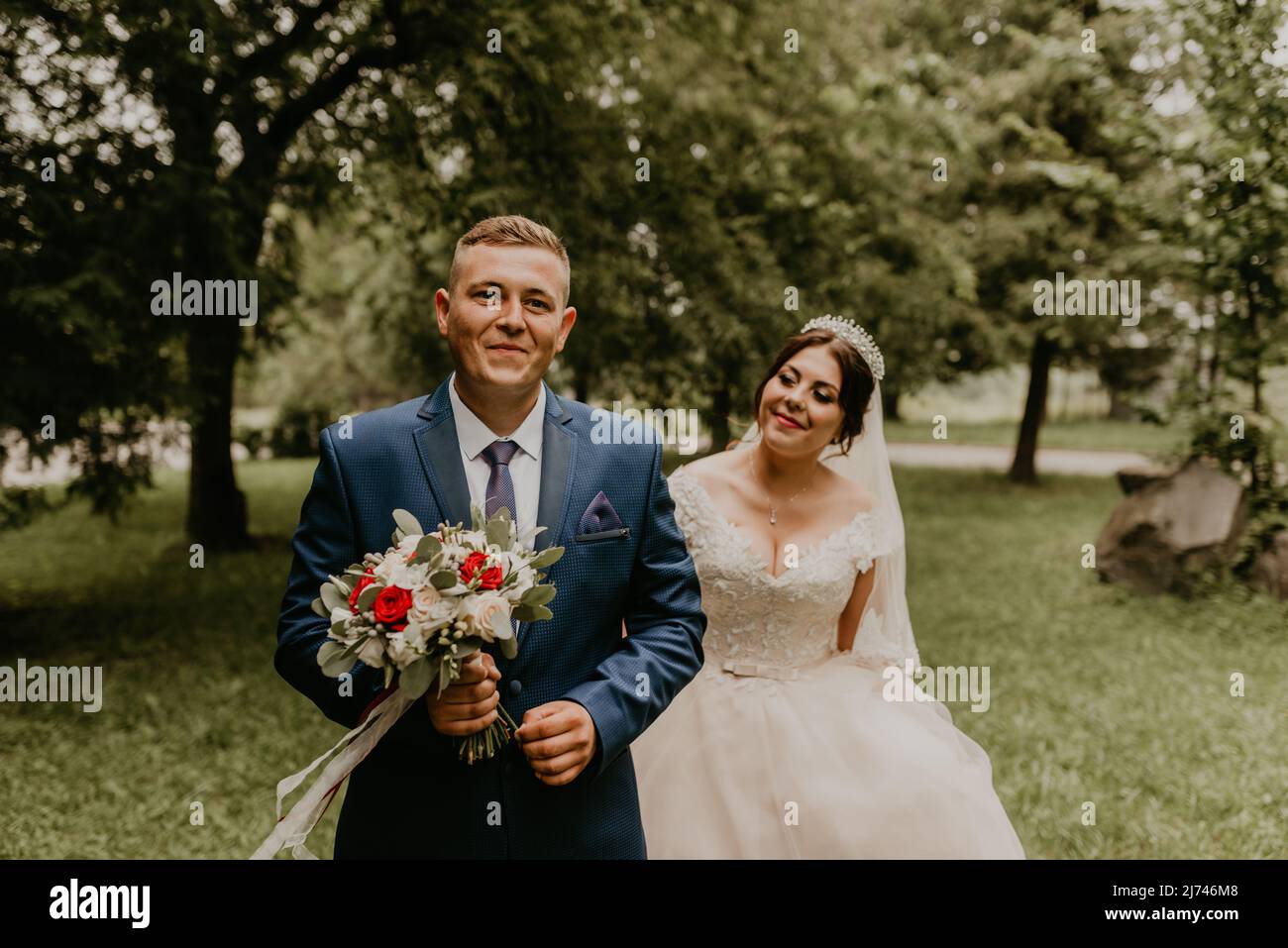 Blonde européenne caucasienne jeune homme marié en costume bleu et femme à cheveux noirs mariée en robe de mariage blanche avec voile long et tiara sur la tête. D'abord Banque D'Images