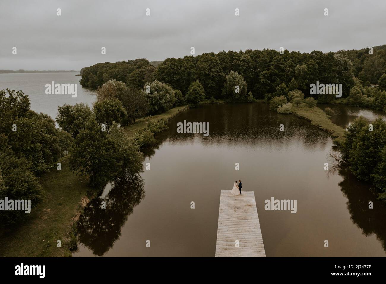 Homme caucasien européen marié en costume et femme à cheveux noirs mariée en robe de mariage blanche avec voile long et tiara sur la tête. Les jeunes mariés s'embrasent Banque D'Images