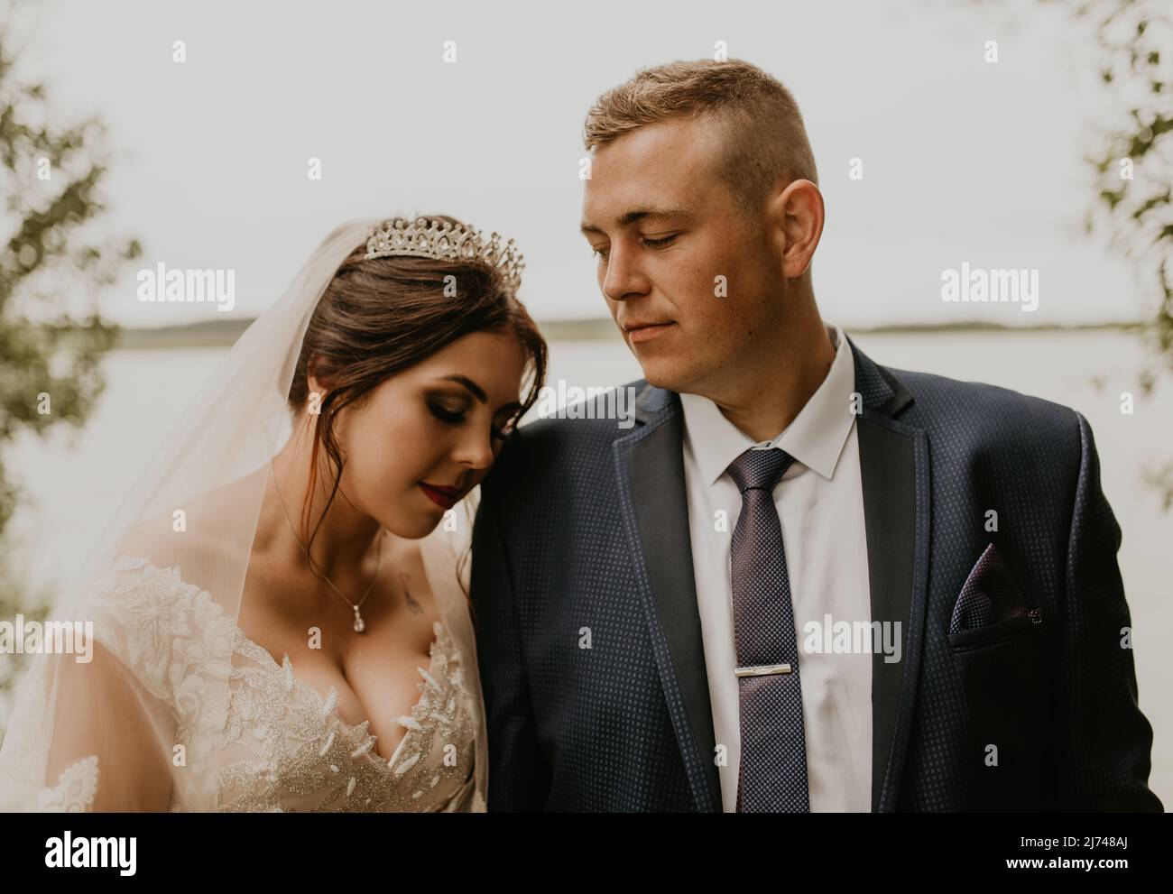 Blonde européenne caucasienne jeune homme marié en costume bleu et femme à cheveux noirs mariée en robe de mariage blanche avec voile long et tiara sur la tête. Nouveaux mariés Banque D'Images