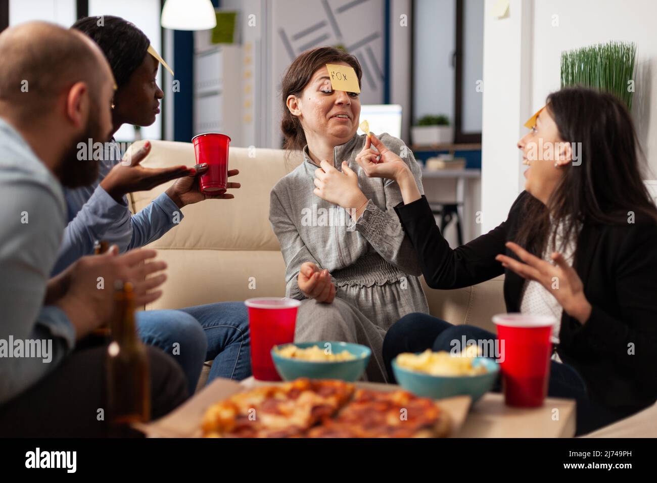 Groupe diversifié de collègues jouant deviner qui jeu avec des notes adhésives sur le front, appréciant l'activité amusante avec des charades jouer. Les gens devinrent le pantomime à la fête des boissons après les heures de travail. Banque D'Images