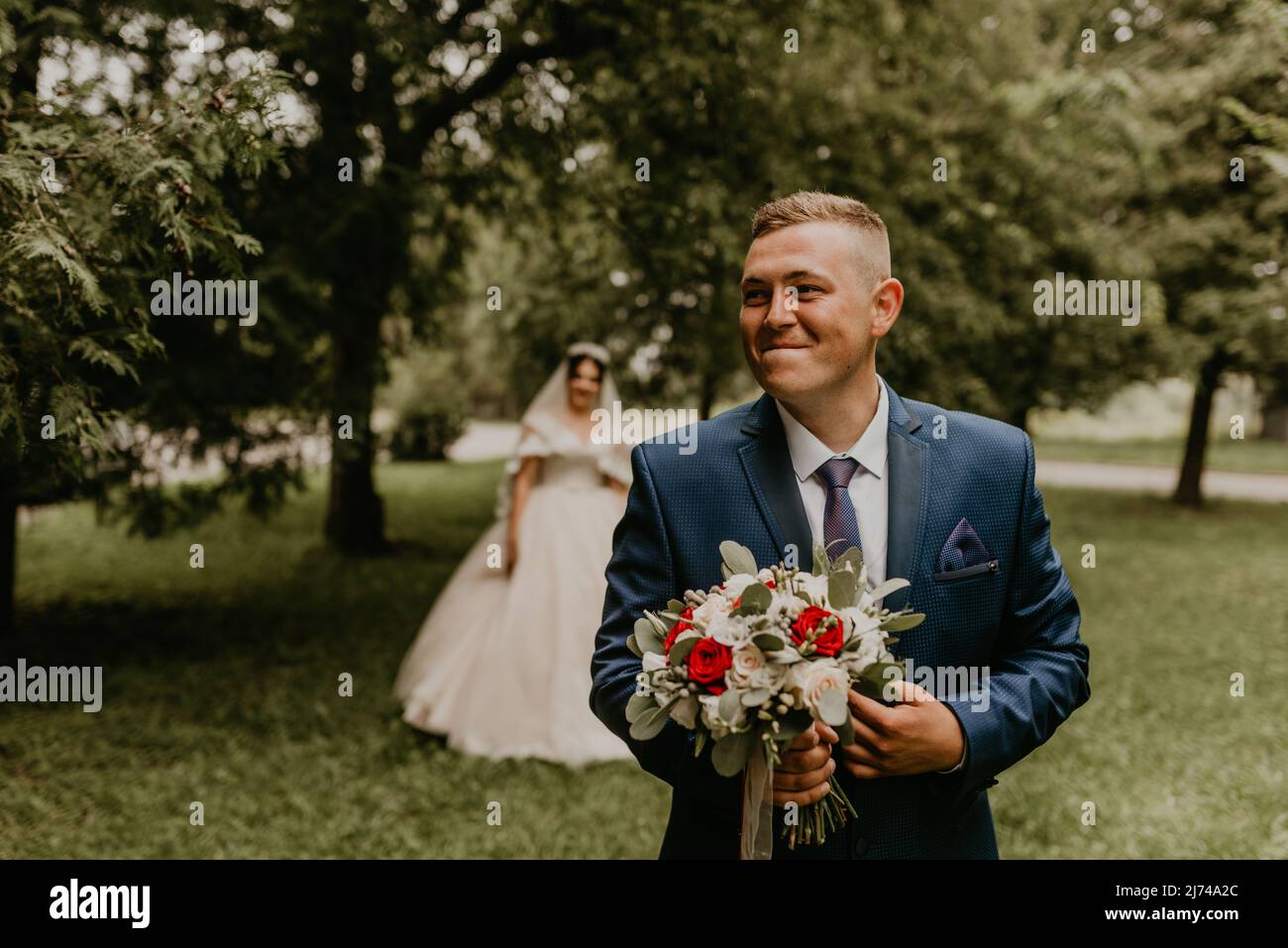 Blonde européenne caucasienne jeune homme marié en costume bleu et femme à cheveux noirs mariée en robe de mariage blanche avec voile long et tiara sur la tête. D'abord Banque D'Images