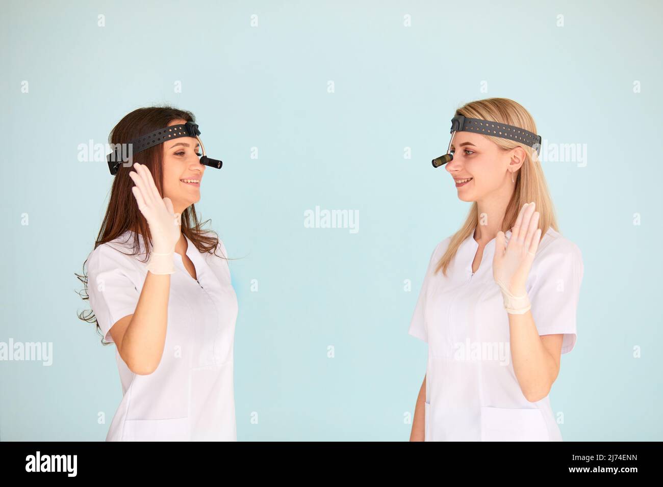 Deux femmes otolaryngologistes sont heureuses du travail qu'elles ont accompli et clament leurs mains sur un fond léger. Concept de protection de la santé Banque D'Images