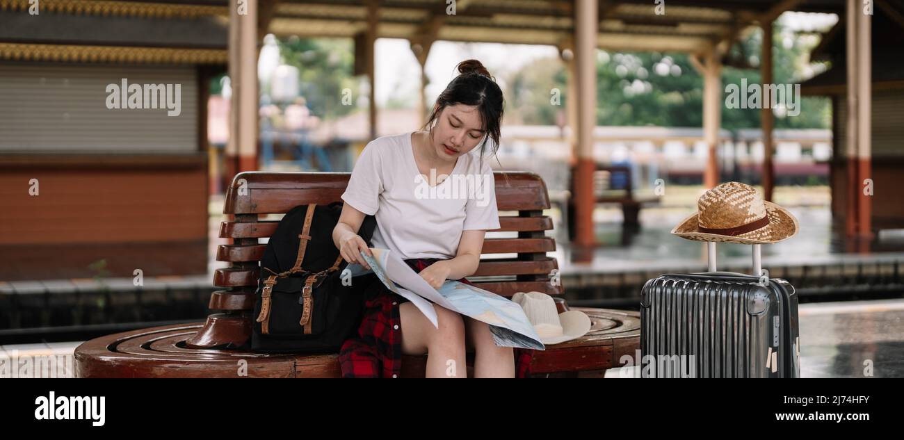 jeune femme asiatique voyageur assis avec une carte choisissez où voyager et sac en attente de train à la gare, concept de voyage d'été Banque D'Images