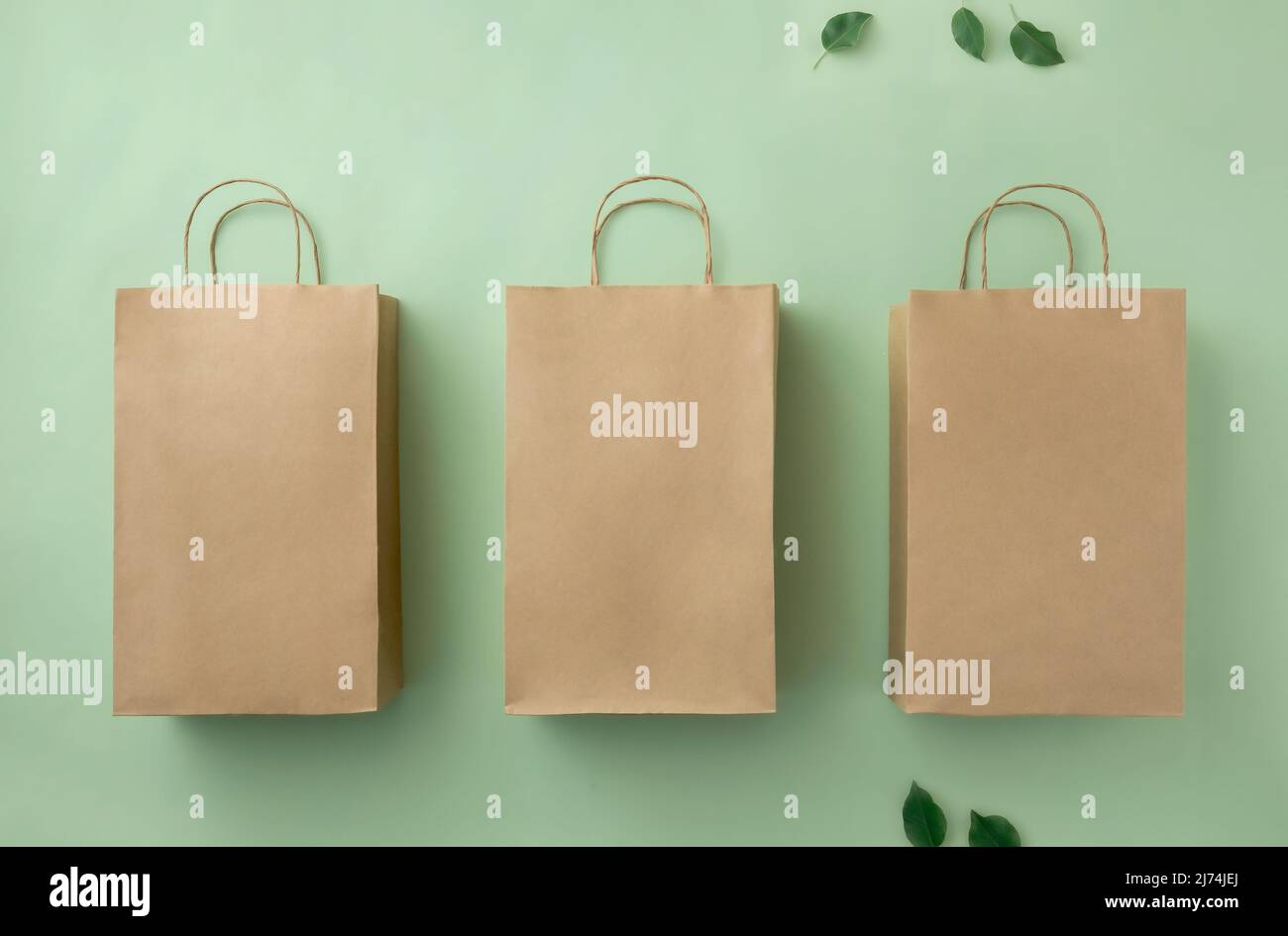 Trois sacs en carton brun sur fond vert et feuilles vertes. Concept d'achat vente et livraison de produit écologique. Banque D'Images