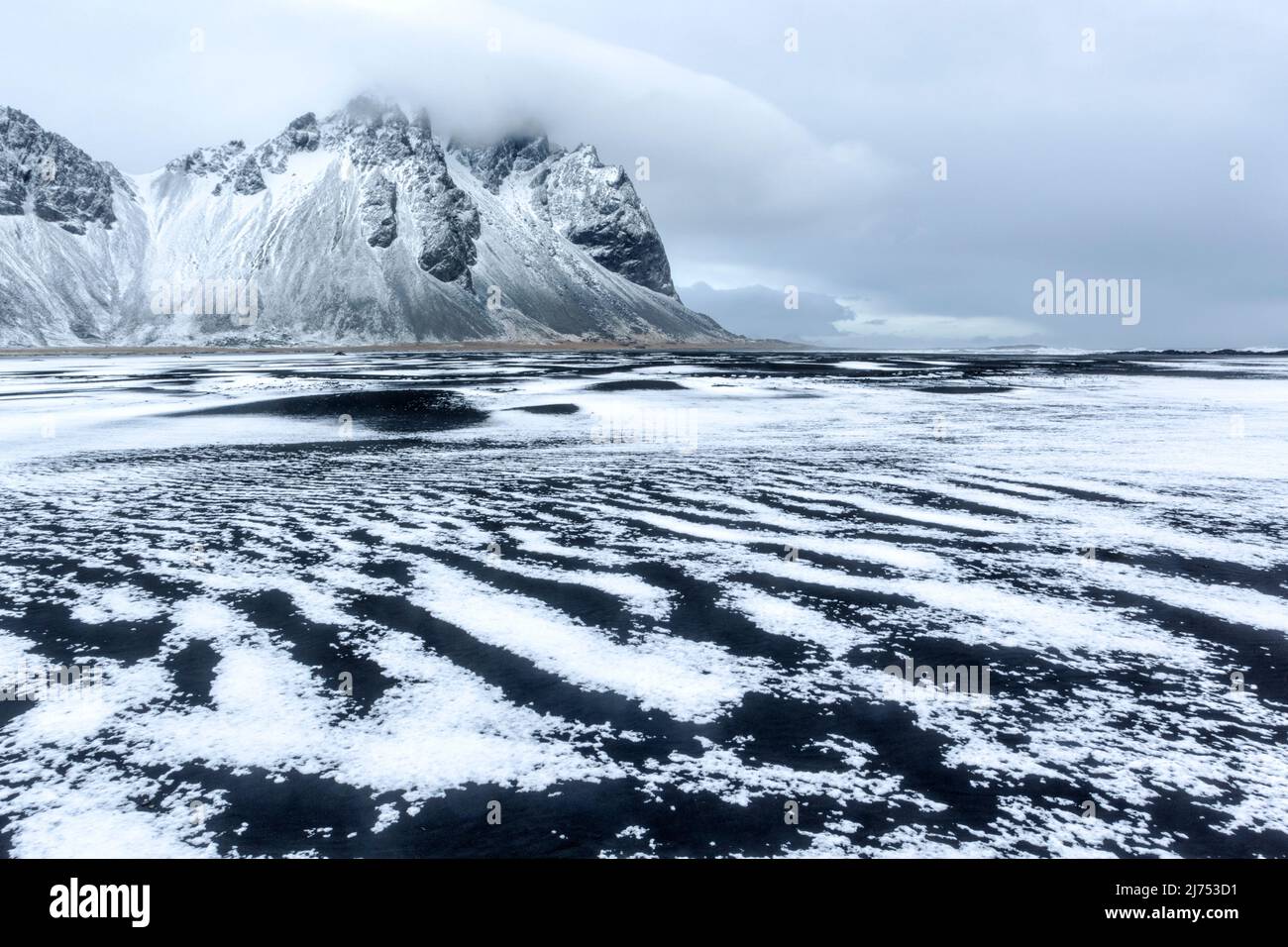 Vue d'hiver de la chaîne de montagnes Vestarhorn sur la péninsule de Stokksnes, en Islande, avec une fine couche de neige et de glace au premier plan. Banque D'Images