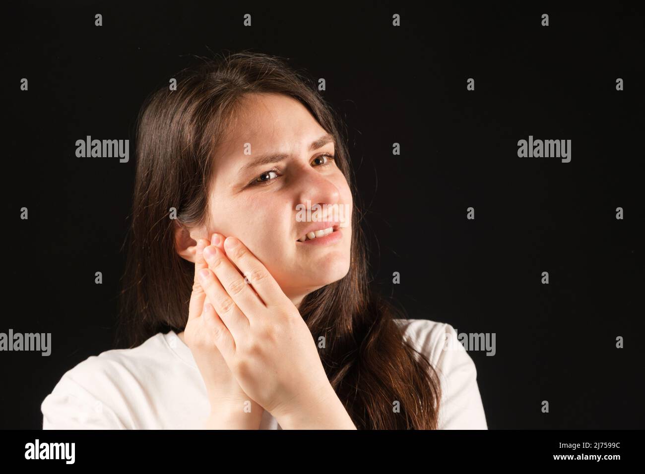 Une femme tient ses mains à une articulation temporomandibulaire douloureuse, dysfonctionnement et douleur, mâchoire dislogée, problèmes de dents de sagesse. Banque D'Images