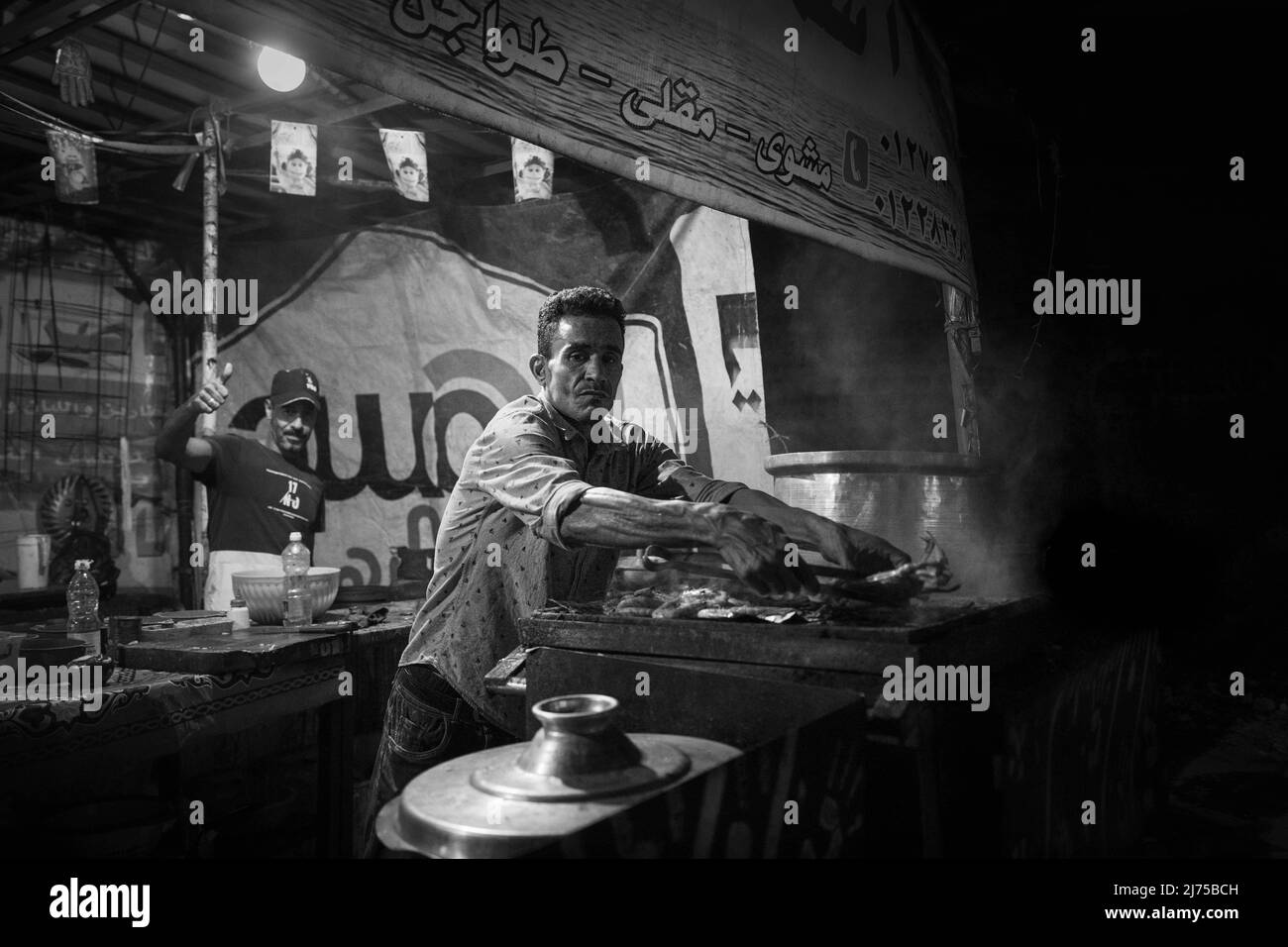 Alexandrie, Egypte - 21 décembre 2021 : un homme fait frire du poisson dans un restaurant de rue la nuit, photo noir et blanc Banque D'Images