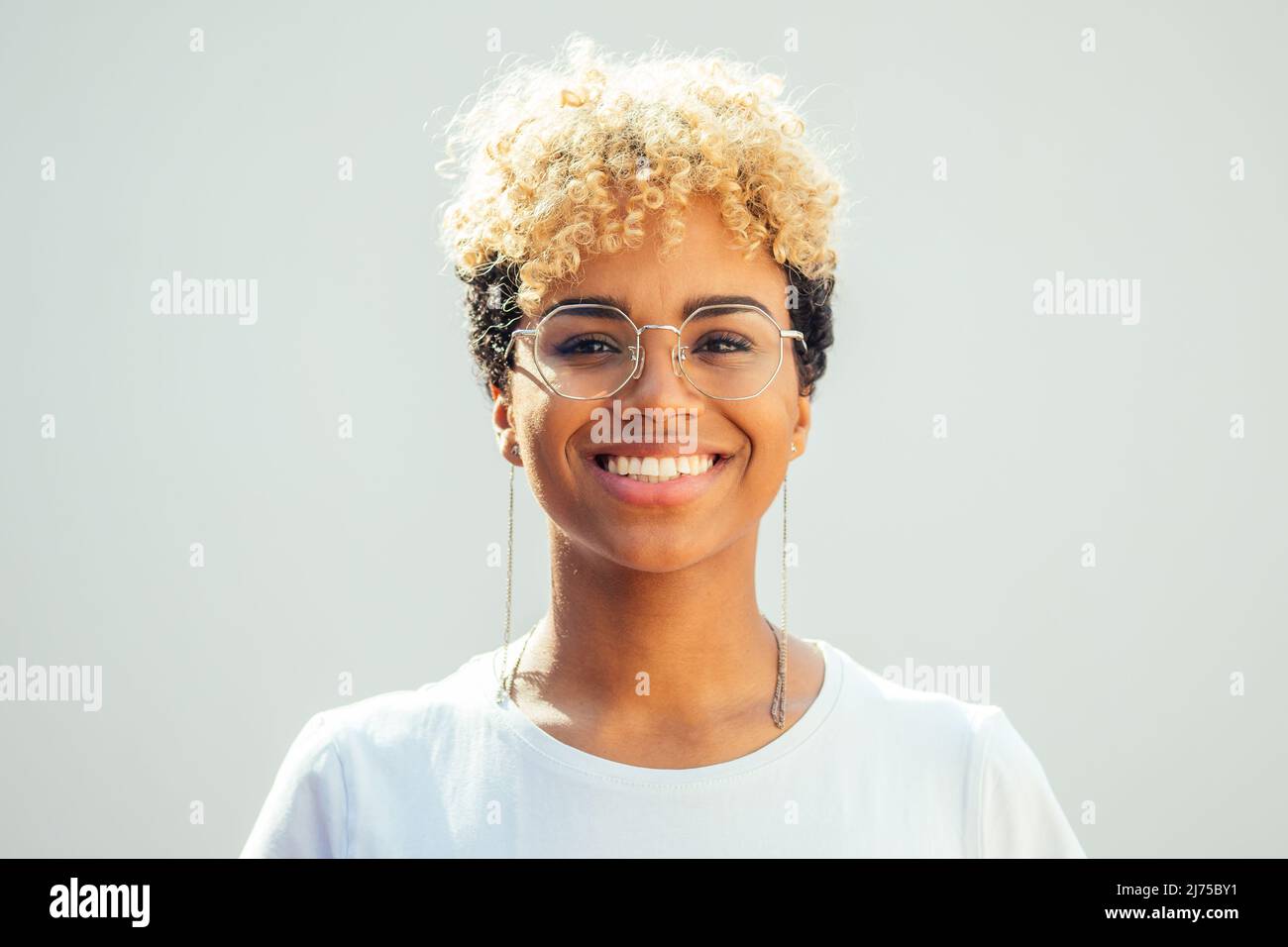 Jeune femme hispanique brésilienne avec des cheveux freux blonds frais regardant à travers des lunettes sur fond blanc Banque D'Images
