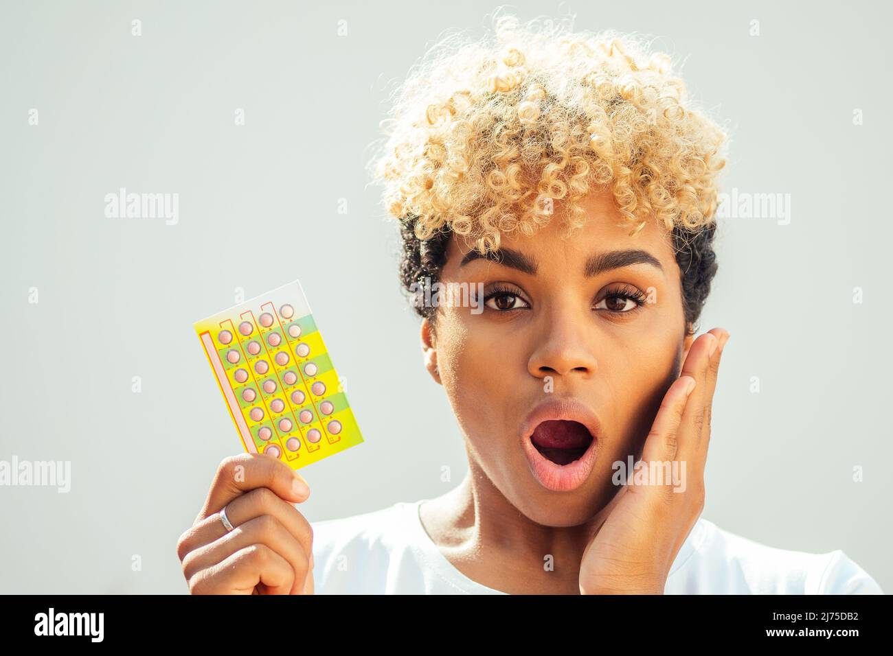 belle surprise afro-américaine femme tenant le comprimé de contrôle de naissance et la bouche ouverte se lance elle a oublié de prendre les pilules à temps. concept de mal de dents Banque D'Images