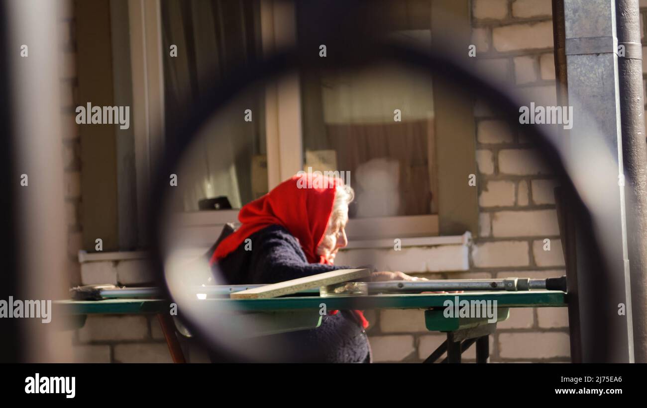 Recentrer la femme âgée ukrainienne dans un châle rouge avec des béquilles assises à l'extérieur. Femme de 85 ans. Personne seule. Face de gros plan. Flou. Des gens tristes. Demen Banque D'Images