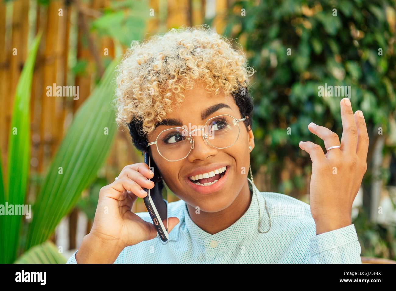 émerveillement blond attrayant cheveux maurly africaine fille américaine commérages avec un ami par téléphone au café tropical Banque D'Images