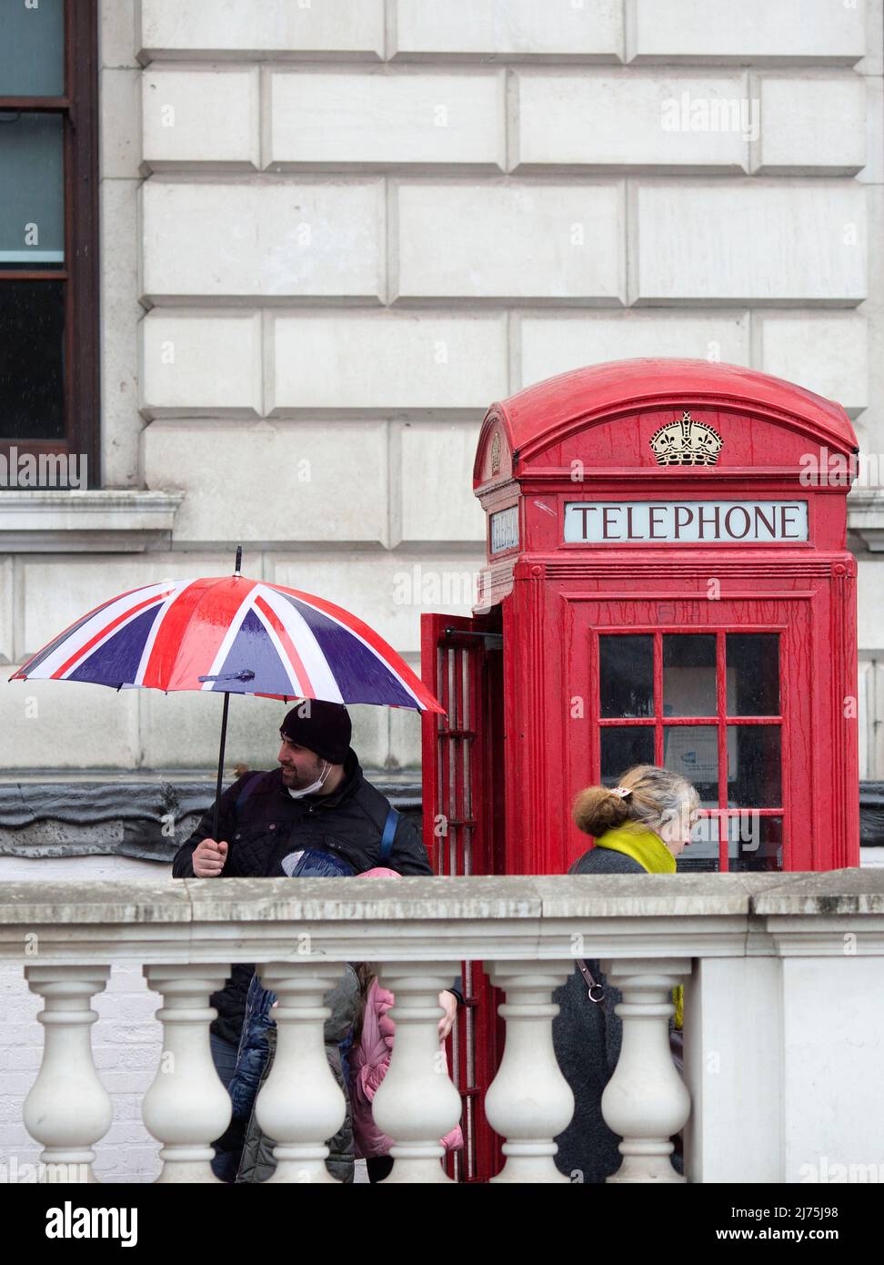 Une personne tient un parapluie drapeau de l'Union à côté d'une boîte téléphonique rouge traditionnelle à Westminster, dans le centre de Londres. Banque D'Images
