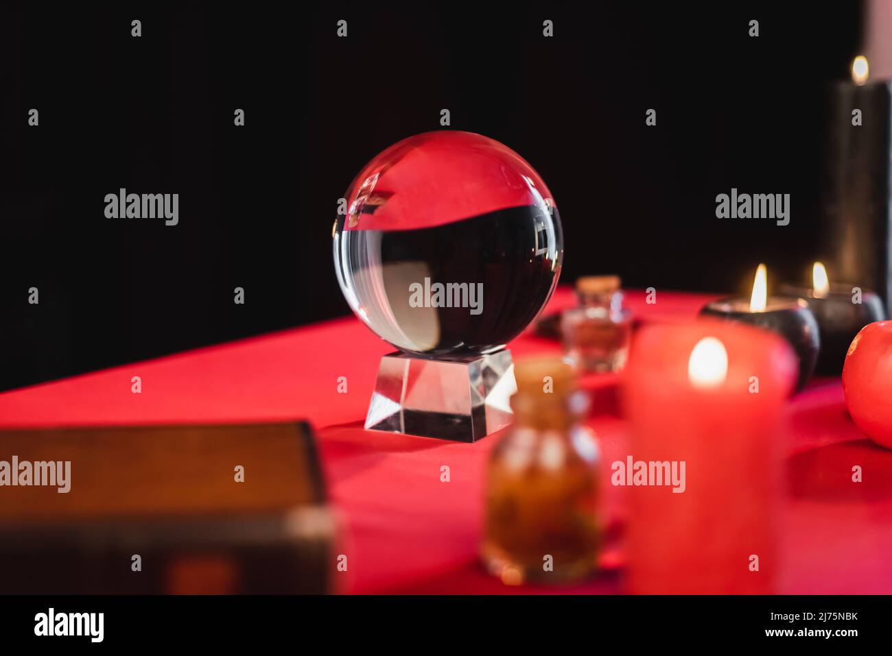 Orbe de verre près de bougies floues et fournitures de sorcellerie sur la table isolée sur noir Banque D'Images