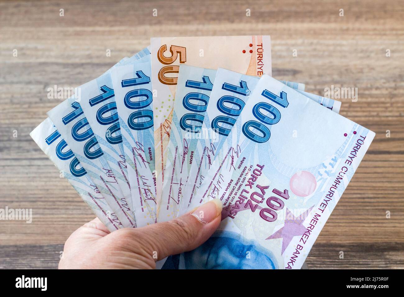 Une main tenant cent cinquante billets turcs sur une surface en bois Banque D'Images
